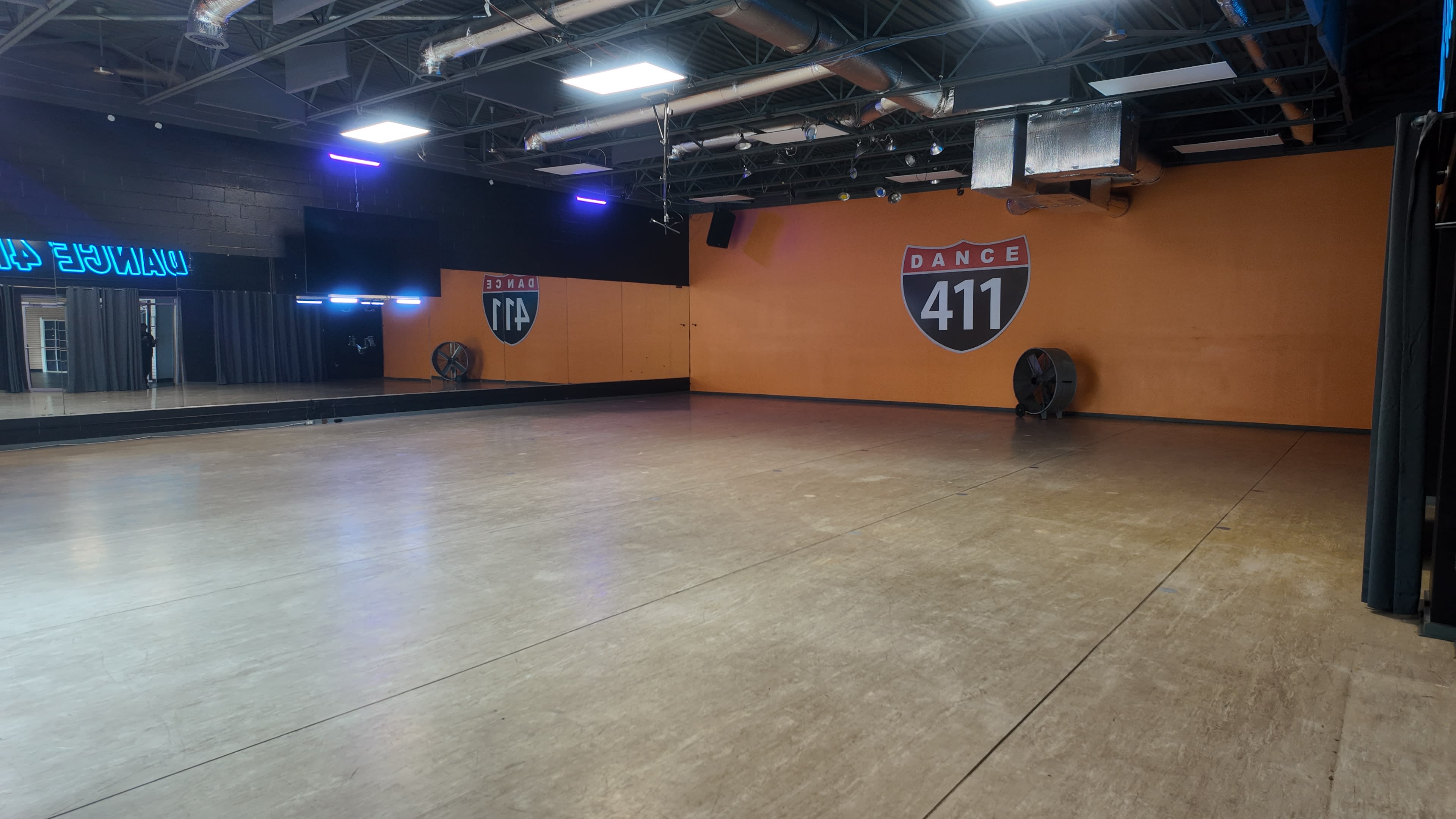 The image shows an empty dance studio with a large mirrored wall, orange accent wall, and signage indicating "Dance 411."