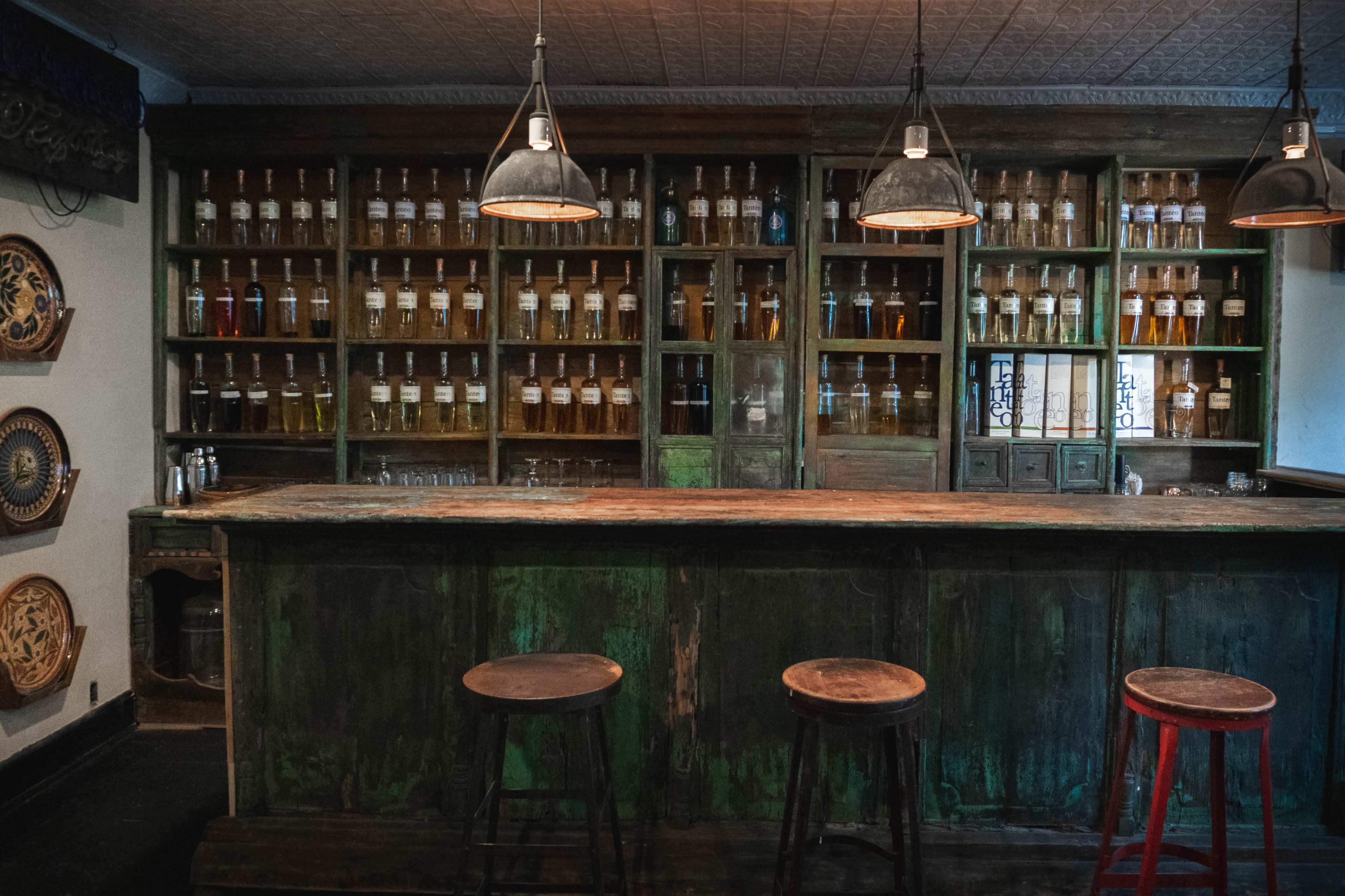A rustic bar feature with a wooden counter and shelves lined with glass bottles in a dimly lit room.