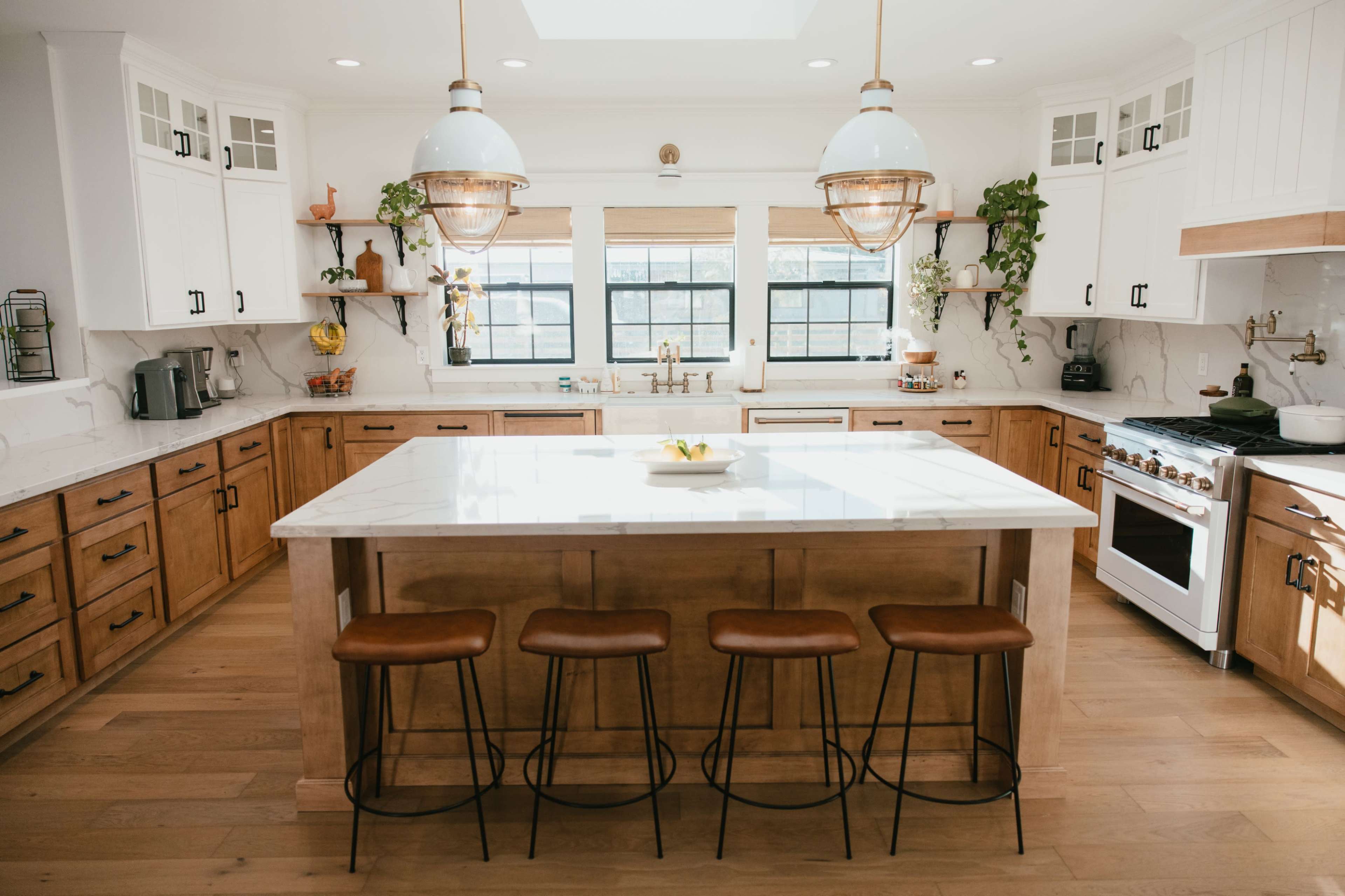 A modern kitchen features a large island with four stools, wooden cabinets, and pendant lighting above, creating a bright and functional space.