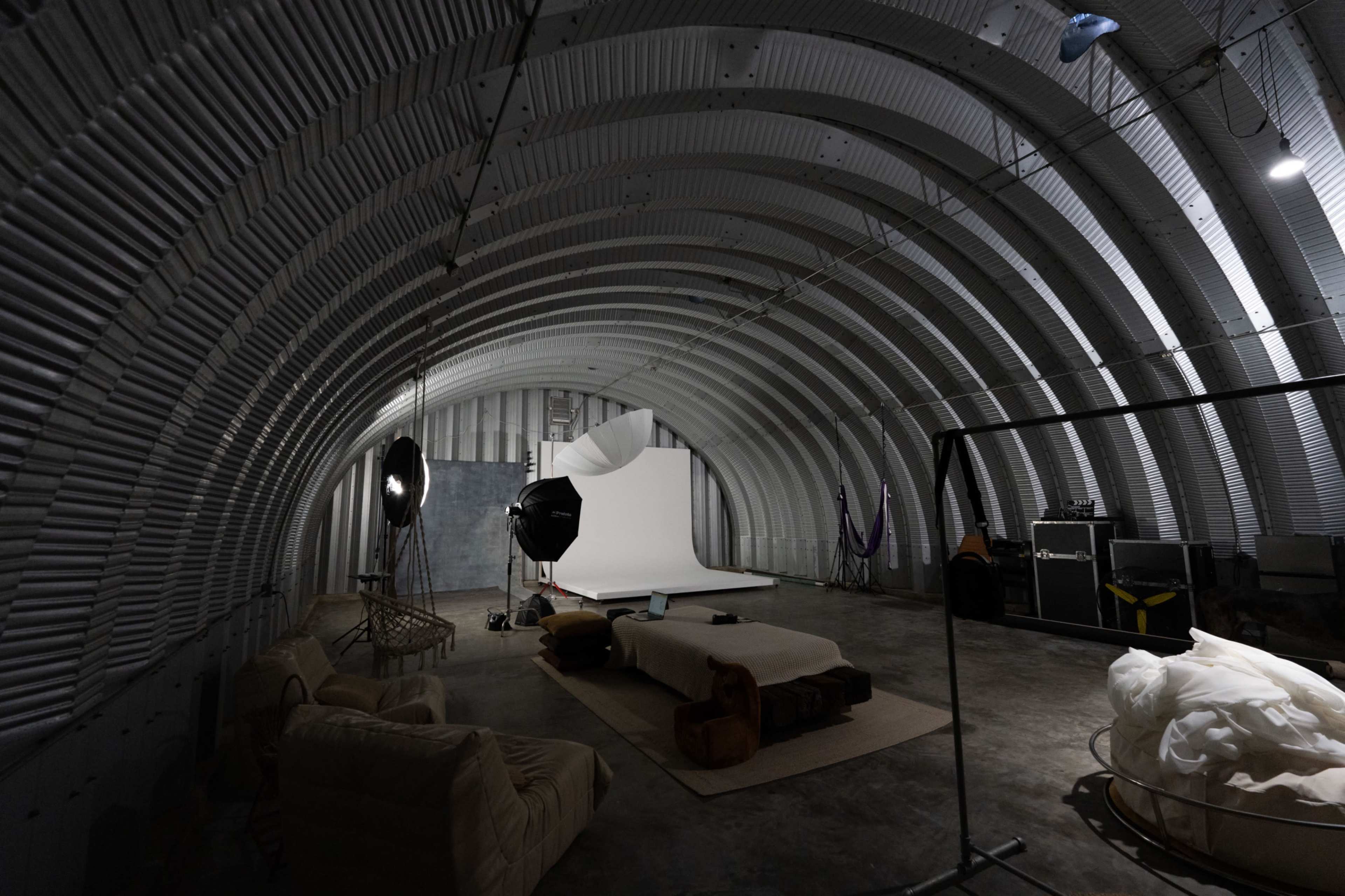 The interior of a curved, industrial space features a photography setup with a backdrop, lighting equipment, and a seating area.