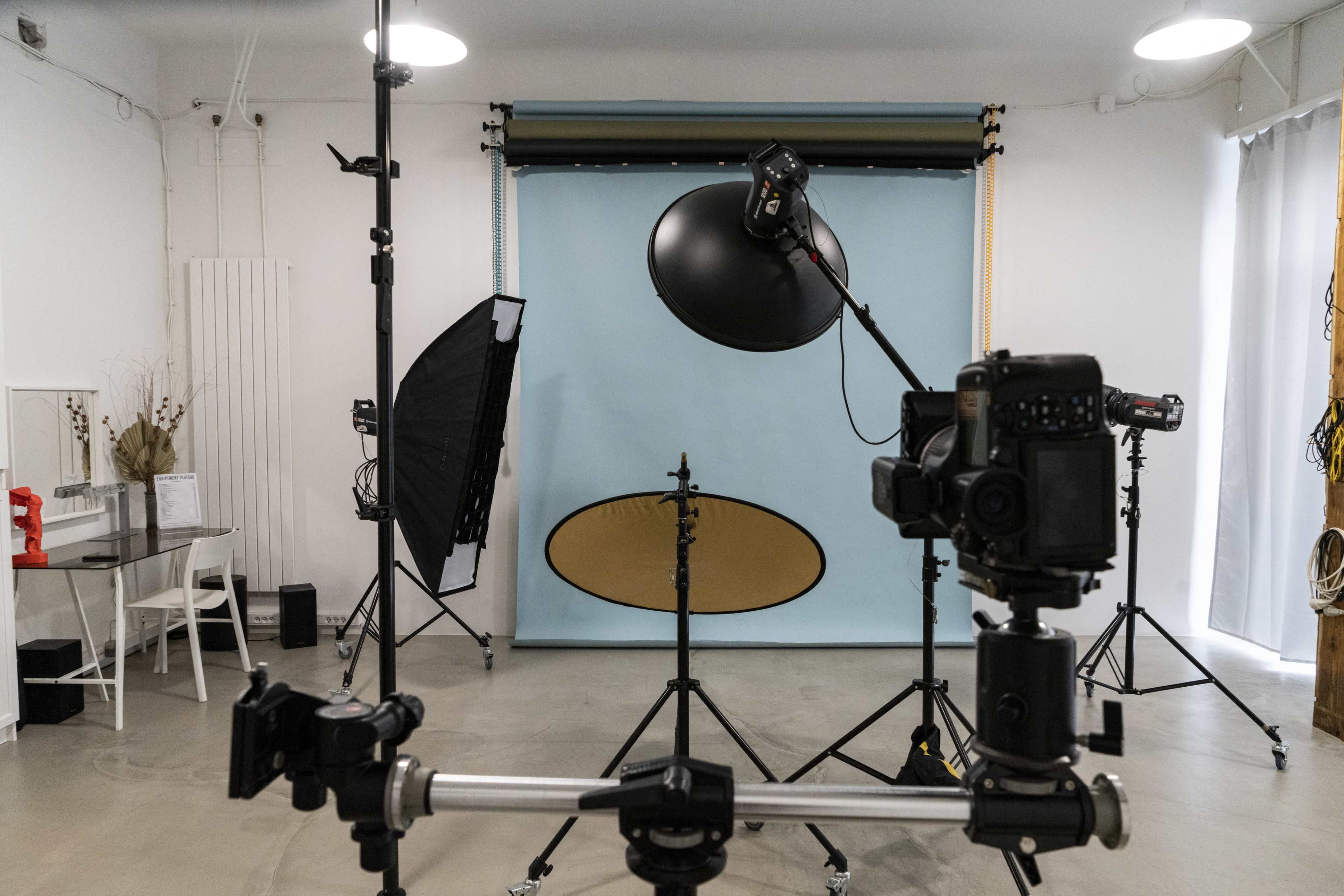 The image shows a photography studio setup with several cameras, lighting equipment, and a blue backdrop.