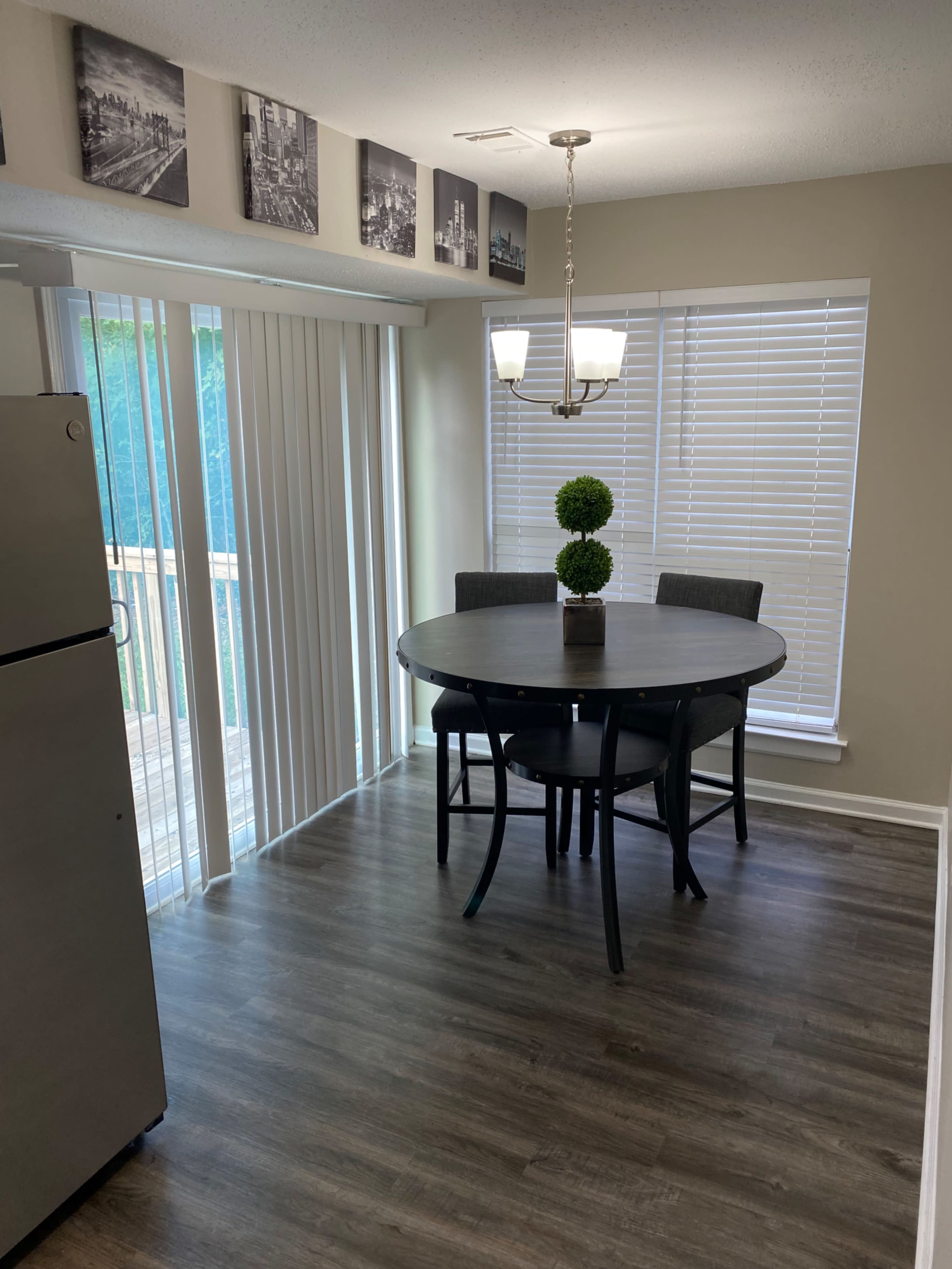 A round dining table with two gray chairs is set in a brightly lit room featuring sliding glass doors and framed black-and-white photographs on the walls.