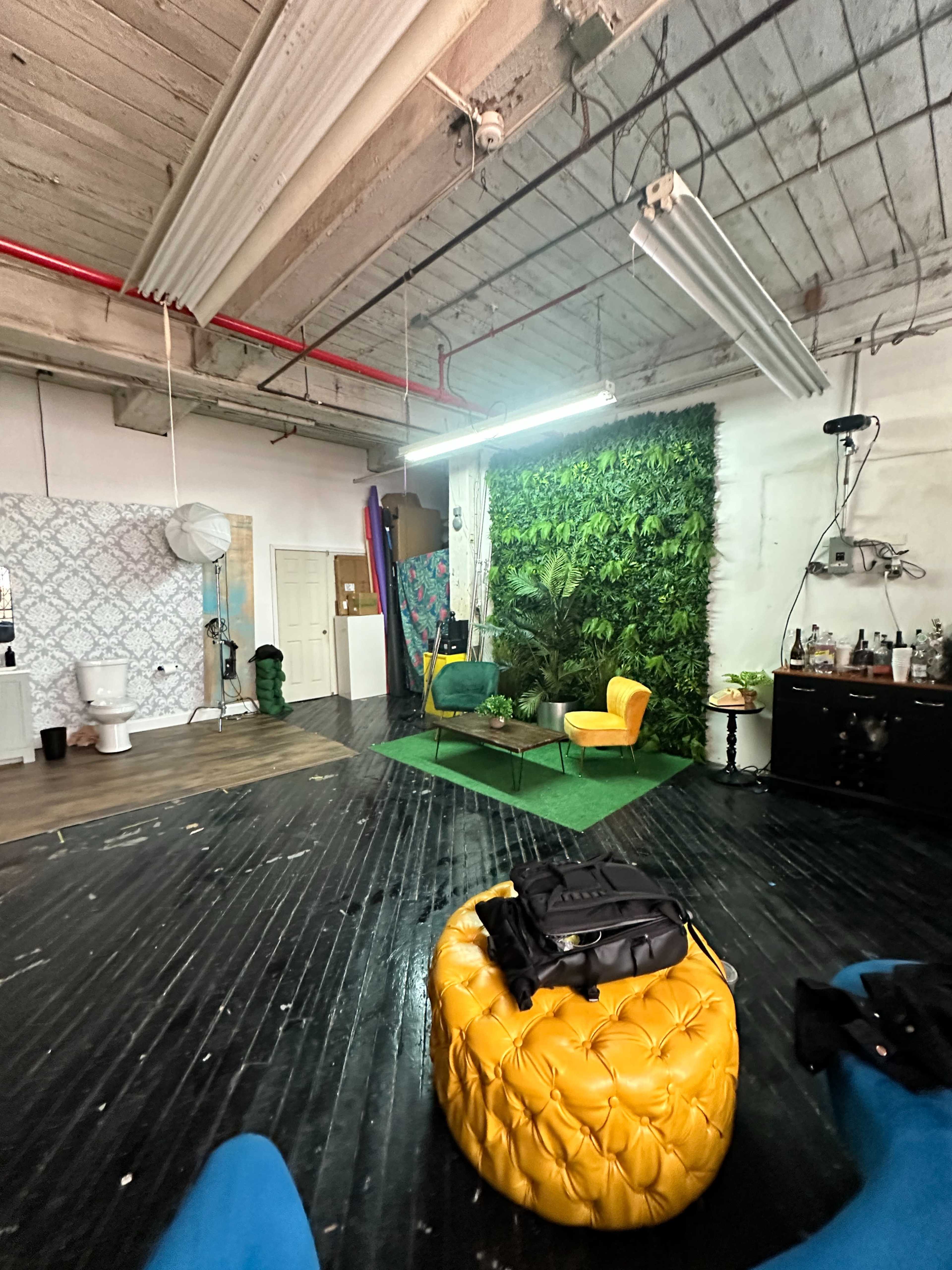 A spacious indoor studio featuring a green wall, two yellow chairs, and a rounded yellow ottoman on a dark wooden floor.