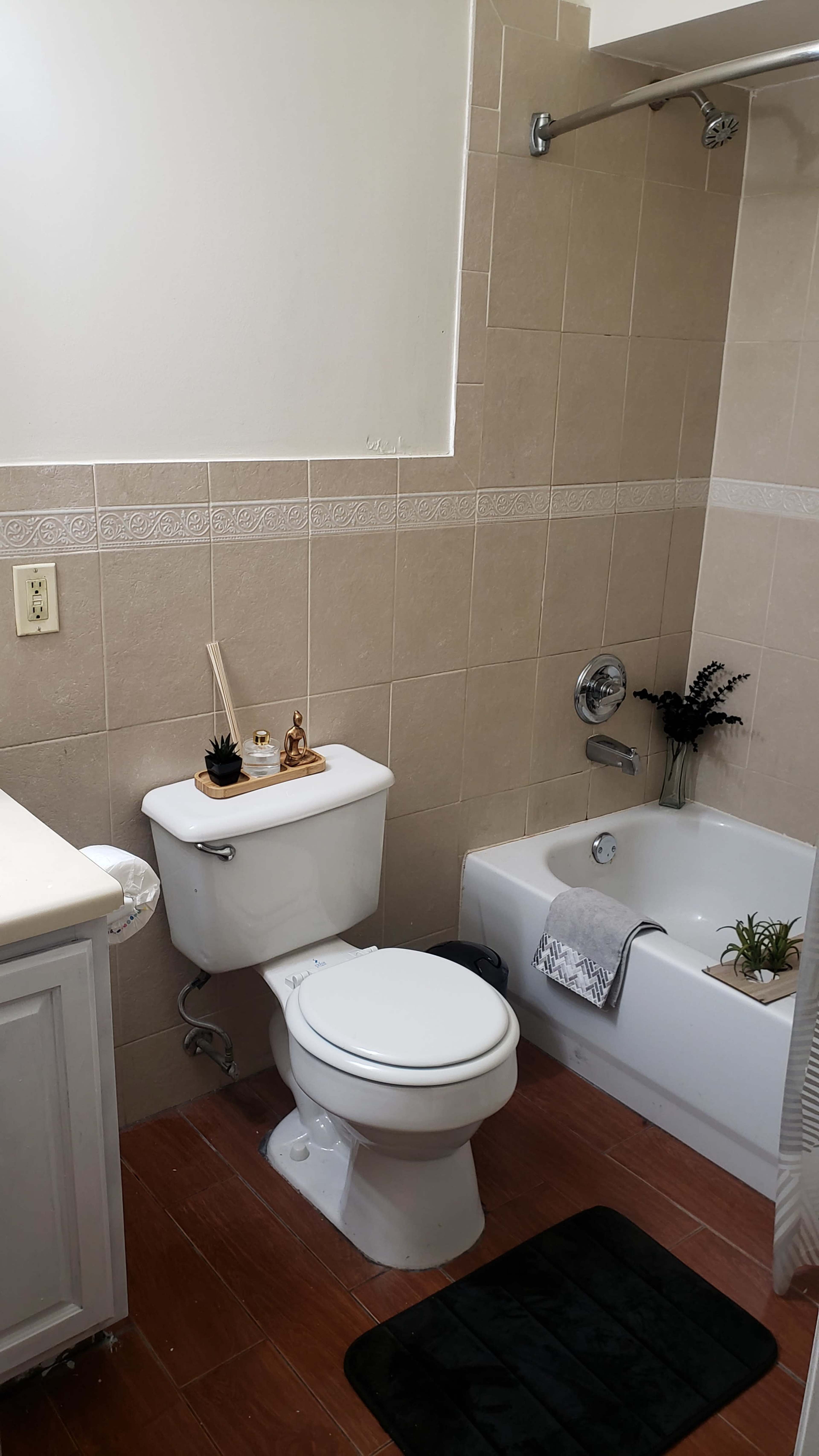 A clean bathroom featuring a toilet, a bathtub with a small plant, a sink with a cabinet, and beige tiled walls.
