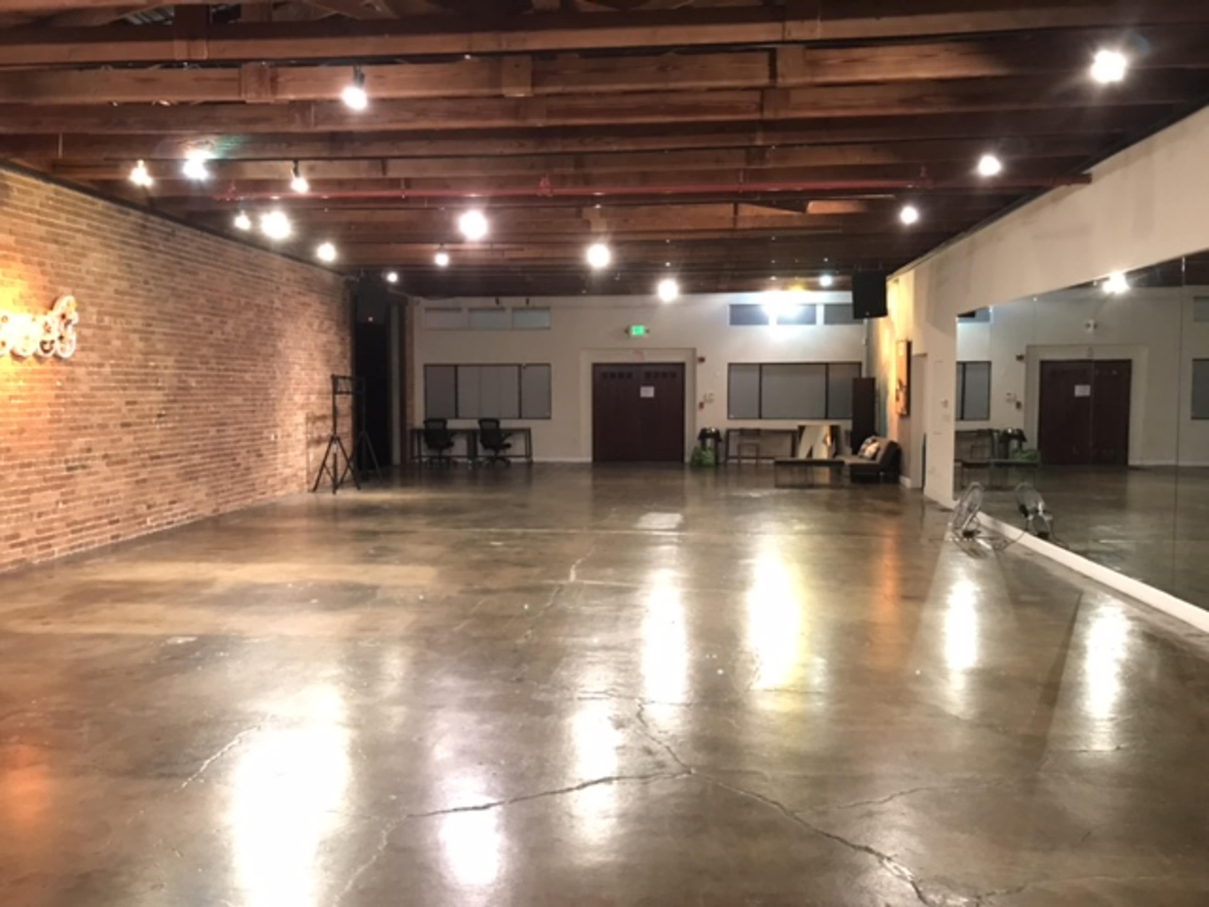 A spacious, empty room with exposed brick walls and polished concrete floors, illuminated by overhead lights.