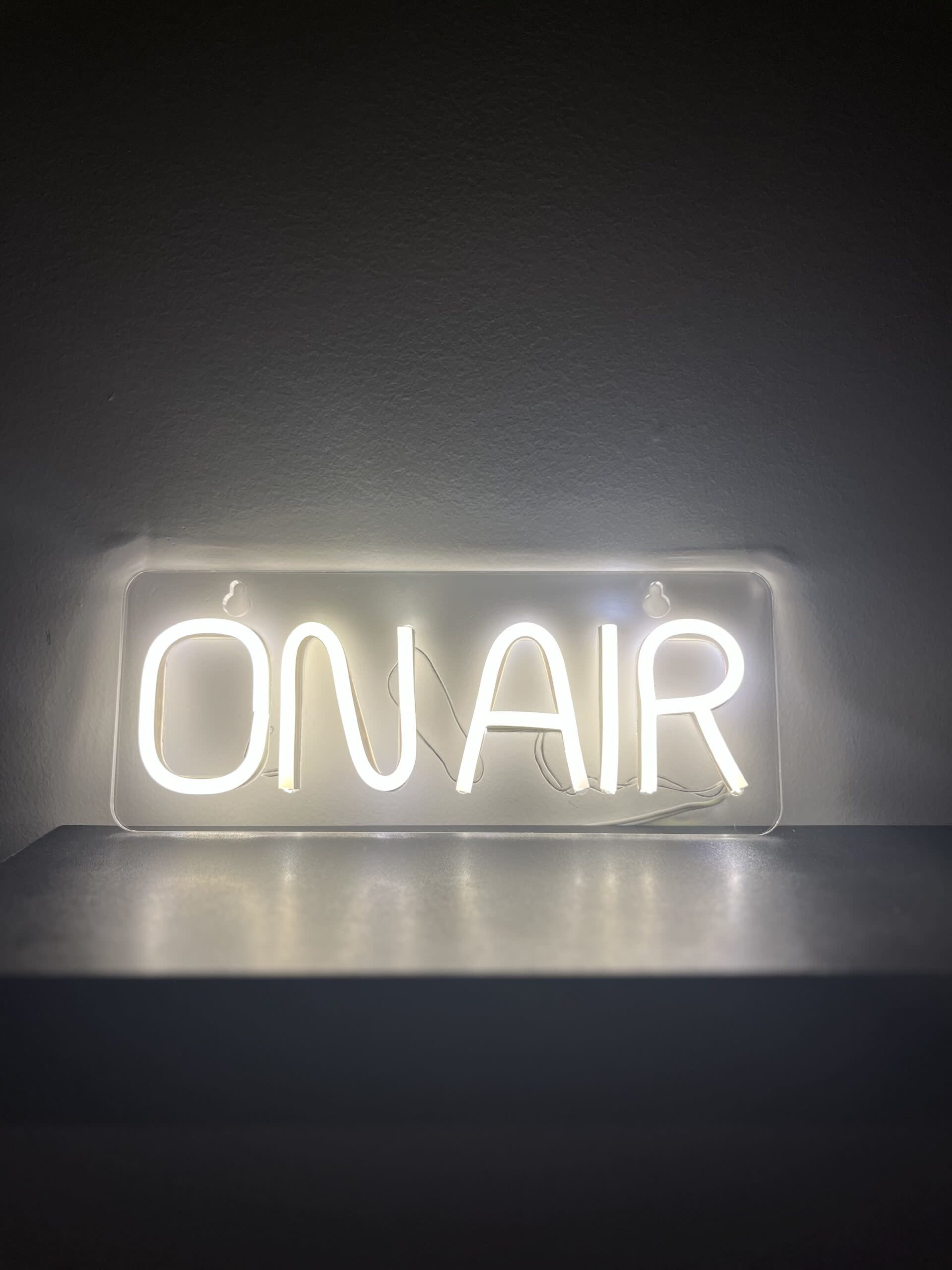 A glowing neon sign displays the words "ON AIR" against a dark background.