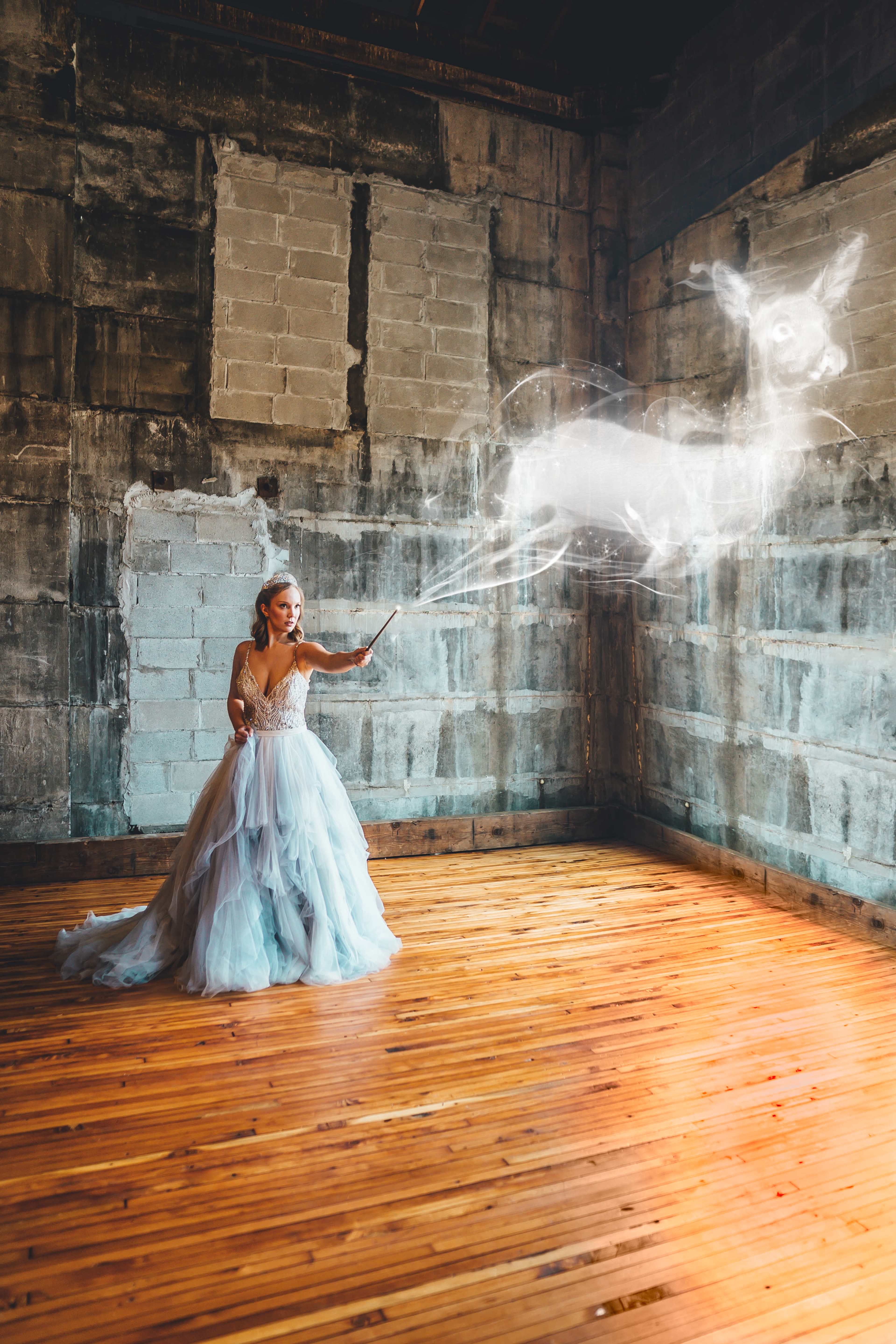 A woman in a flowing dress casts a spell, creating a translucent deer in an empty, rustic room with wooden floors and concrete walls.