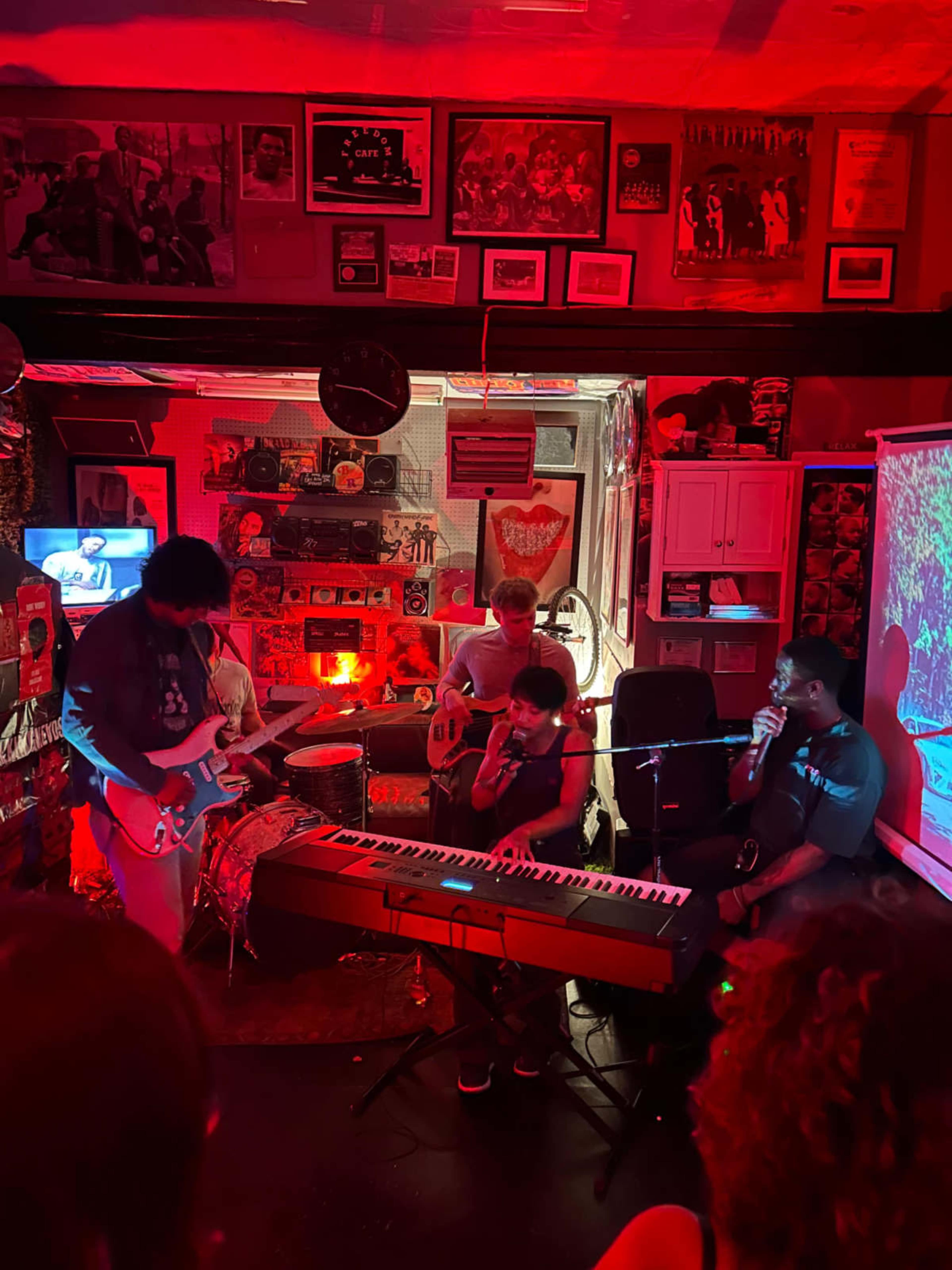 A band performs on a small stage surrounded by colorful decorations, with instruments like a guitar, keyboard, and drums visible.