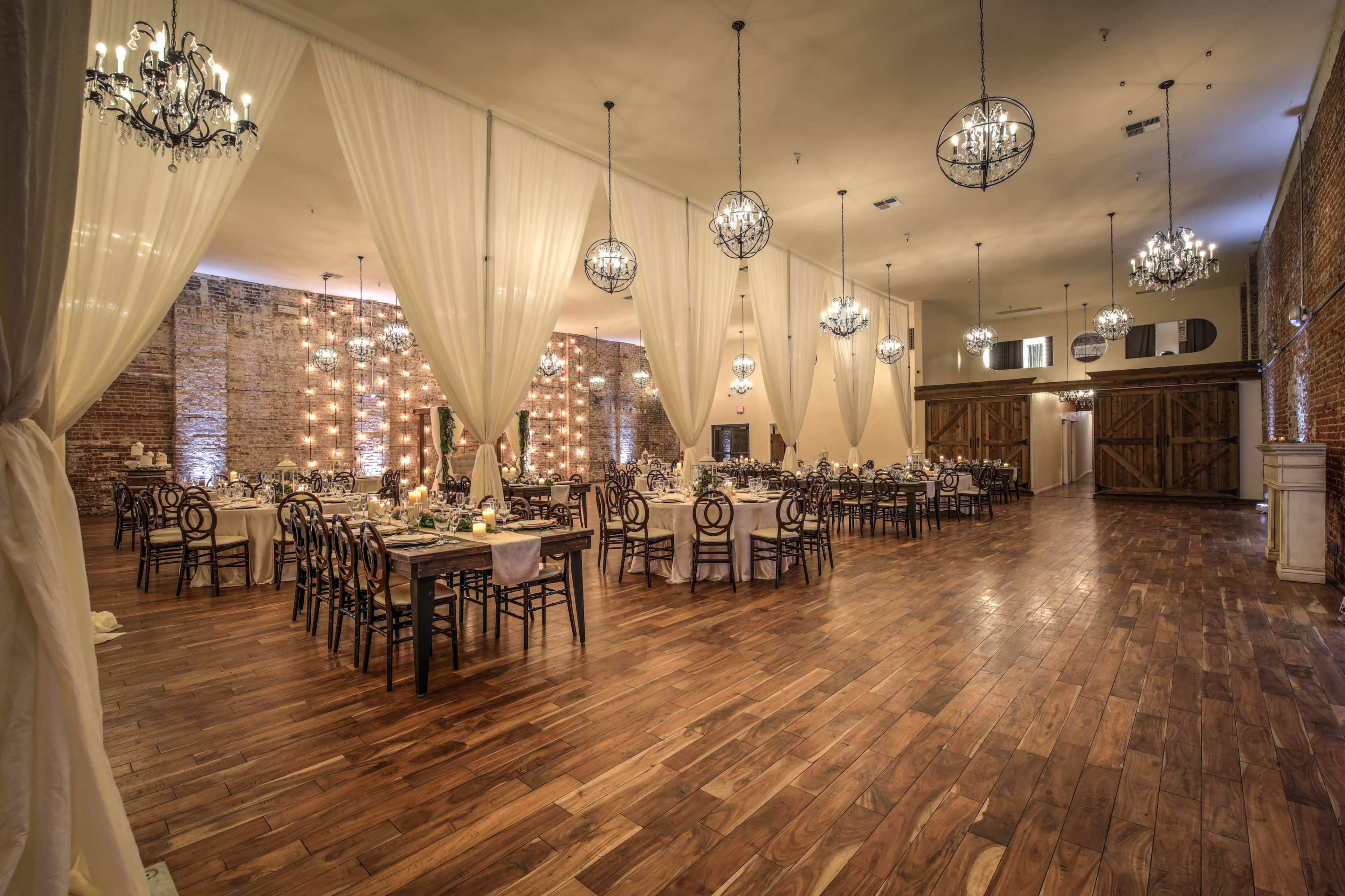 A spacious banquet hall with elegant tables set for dining, adorned by chandeliers and draped fabric partitions.