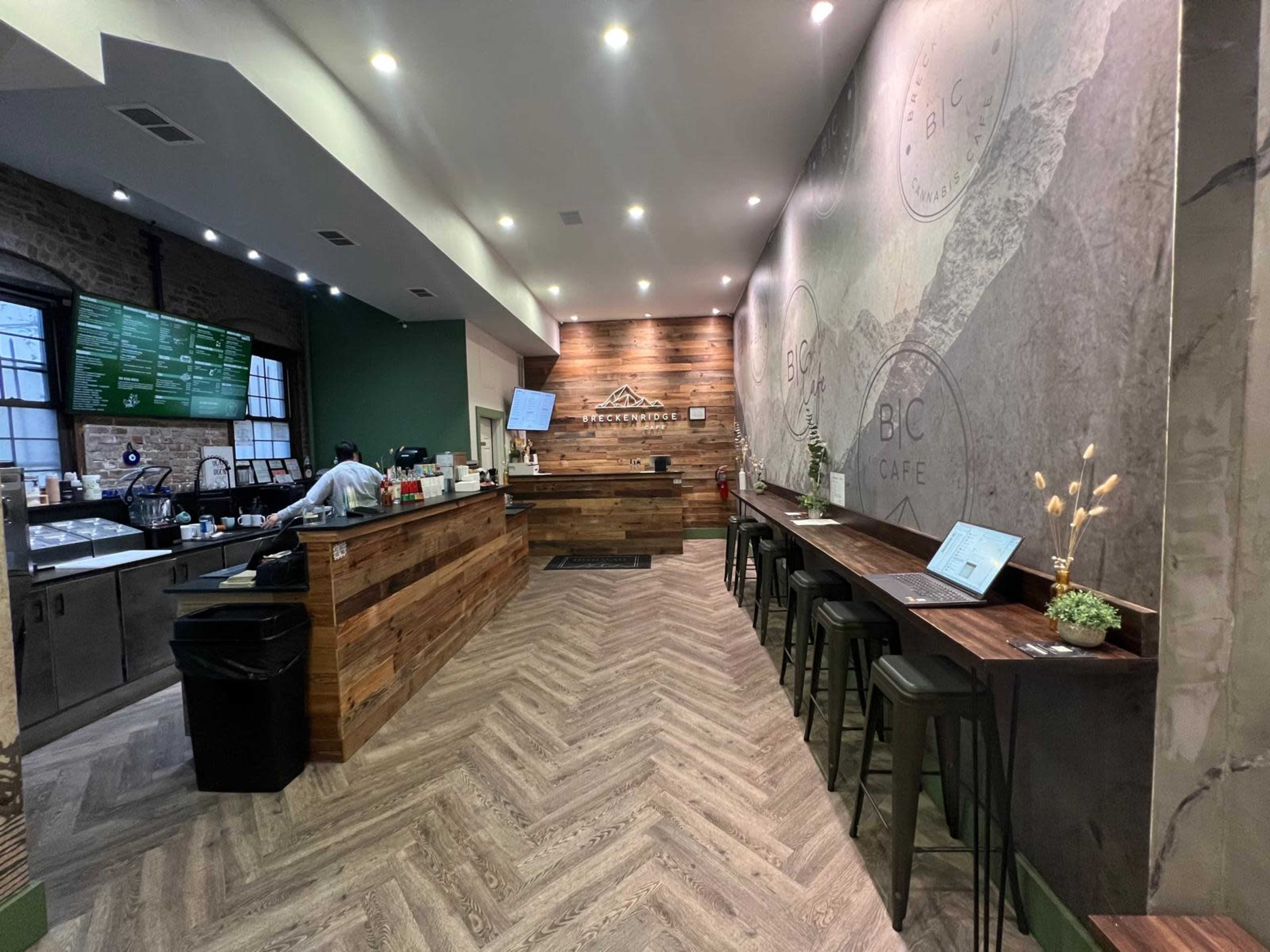 The image shows the interior of a modern café with wooden decor, a service counter, and seating along the walls.