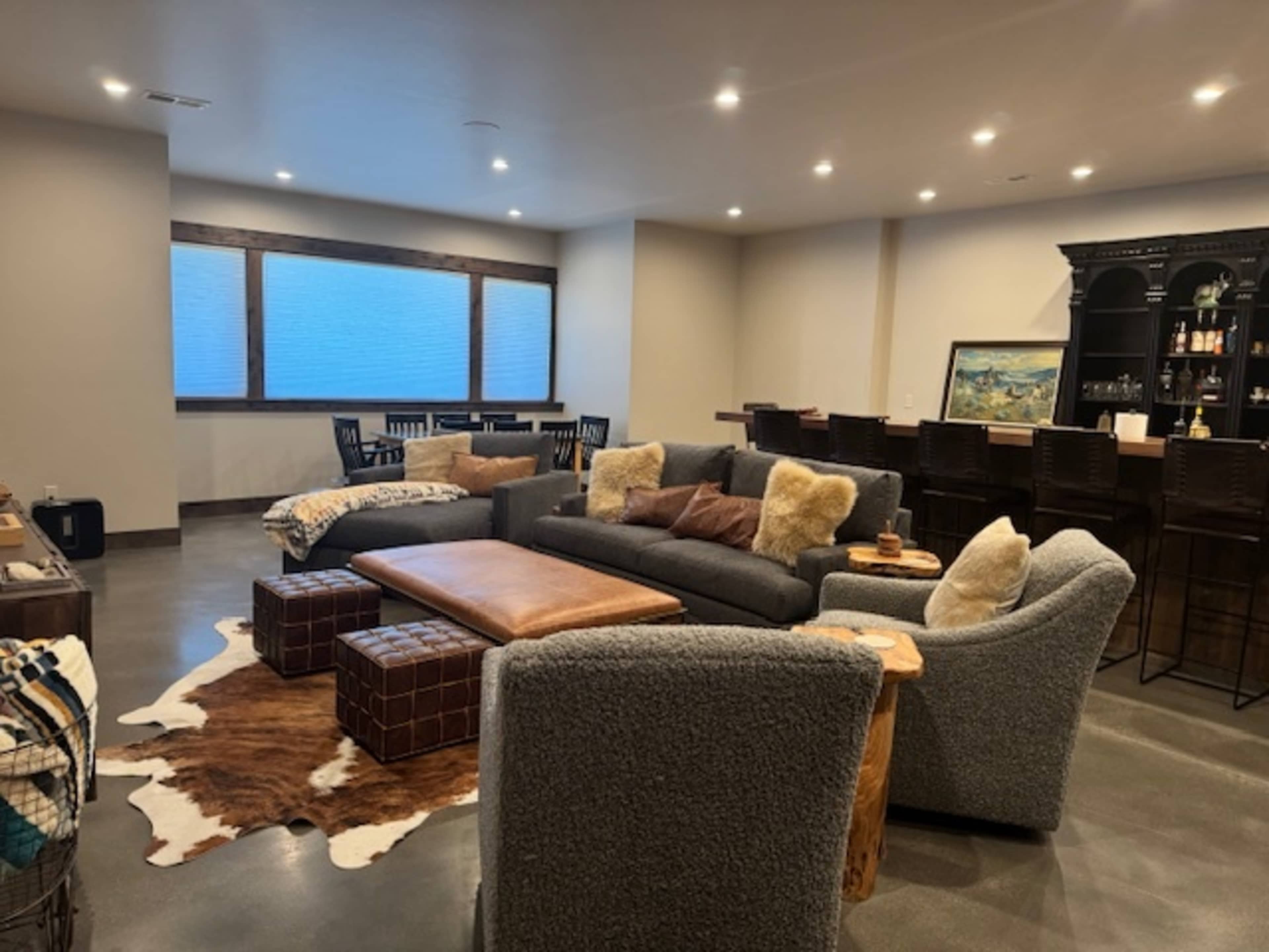 The image shows a modern living room with a large sofa, a coffee table, and a bar area, all illuminated by natural light from windows.