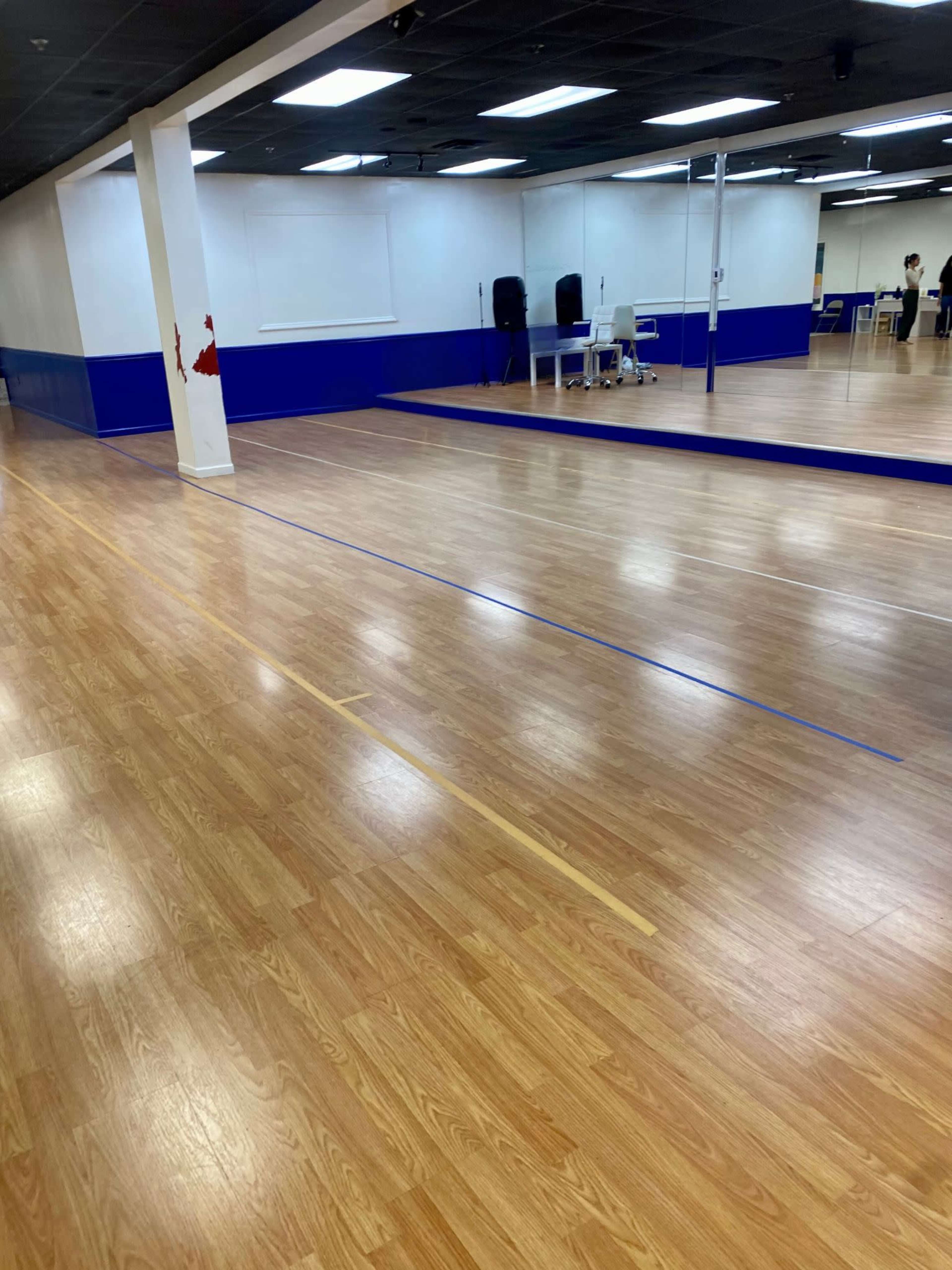 A dance studio with wooden flooring, blue wall accents, and mirrors along one side.