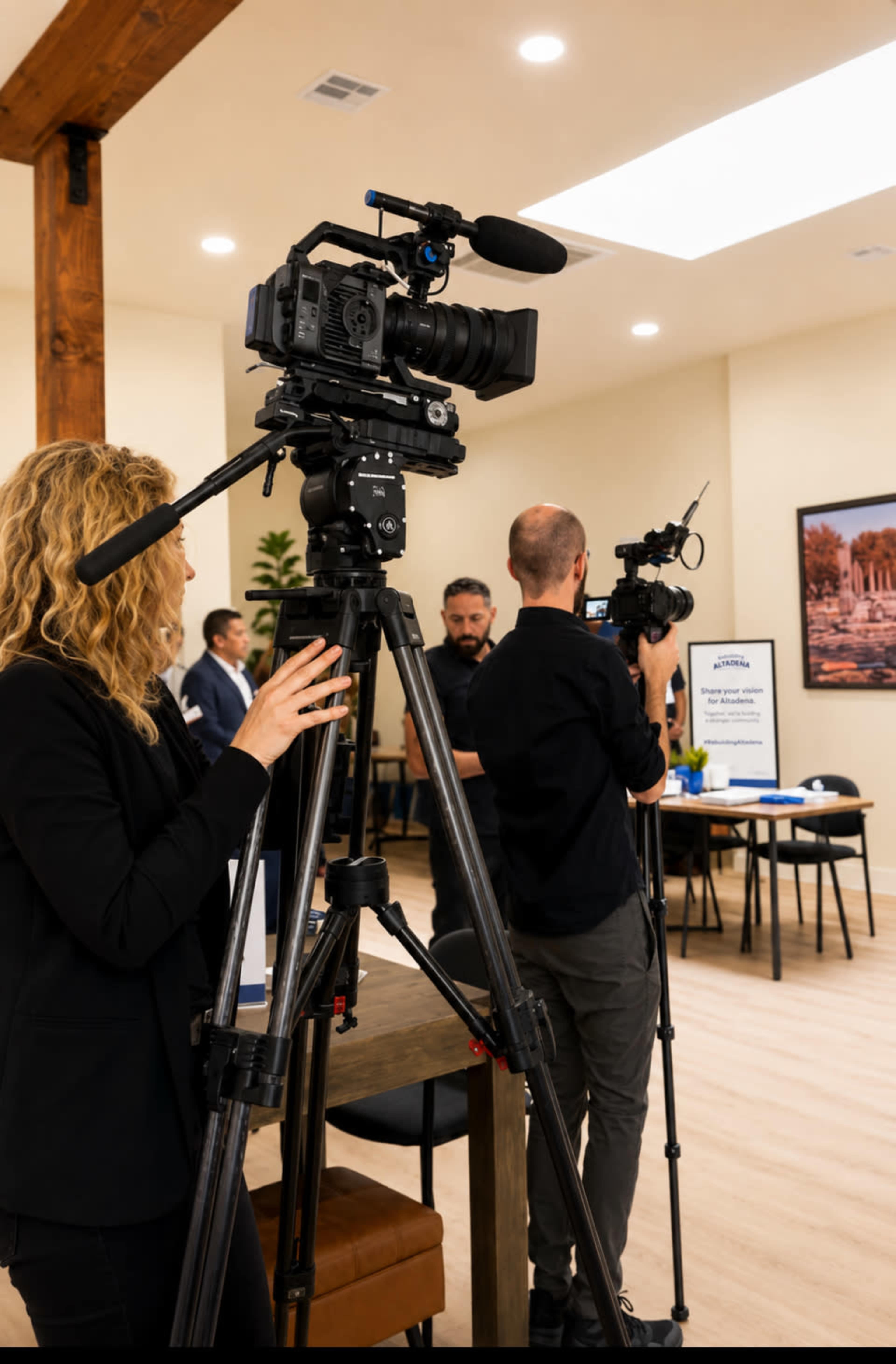 A group of people are setting up cameras on tripods in a well-lit room with tables in the background.