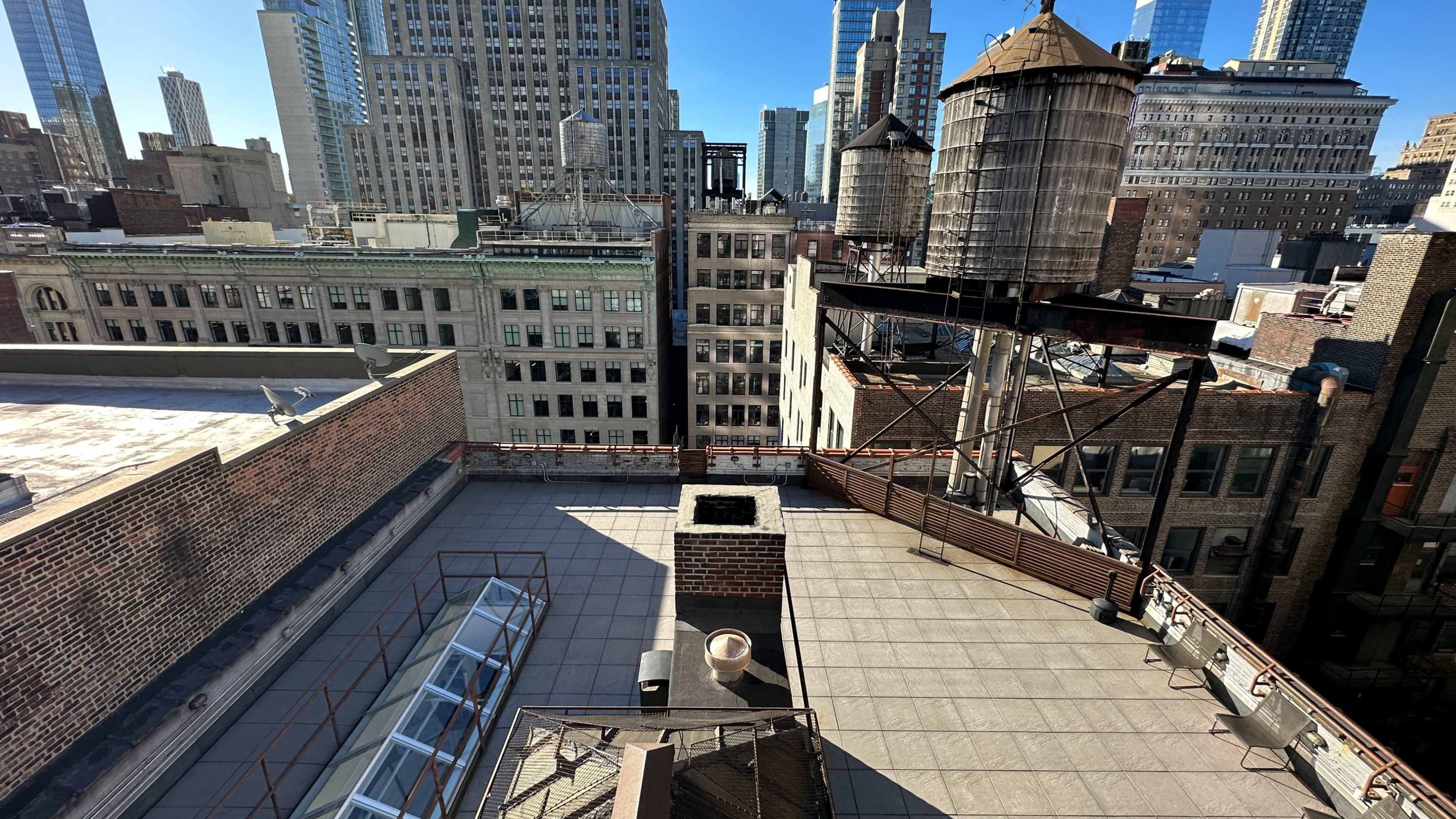 The image shows a rooftop view of a cityscape featuring several buildings, water towers, and a clear blue sky.