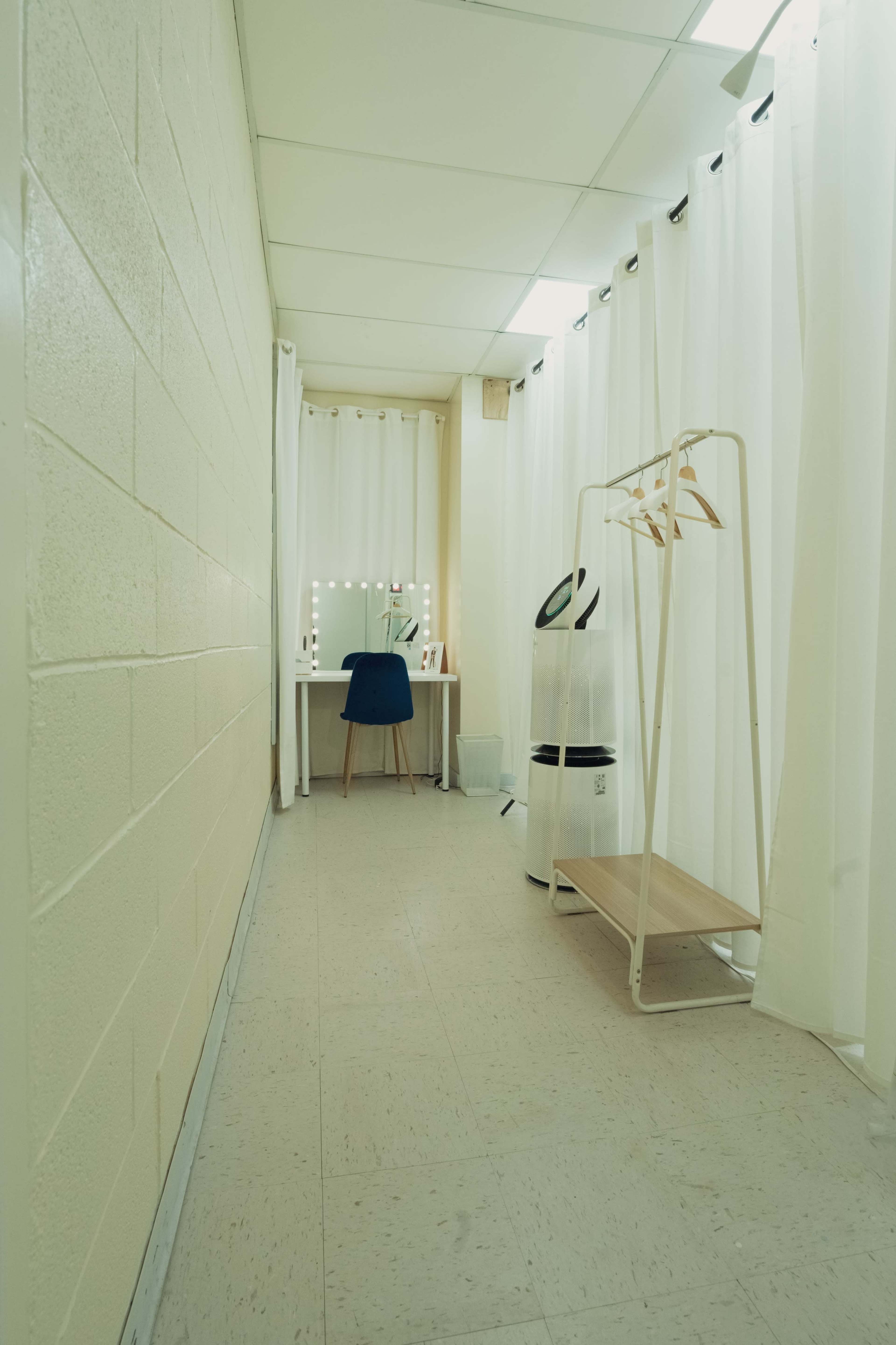 A narrow hallway with a dressing table, a chair, and a clothes rack behind curtains.