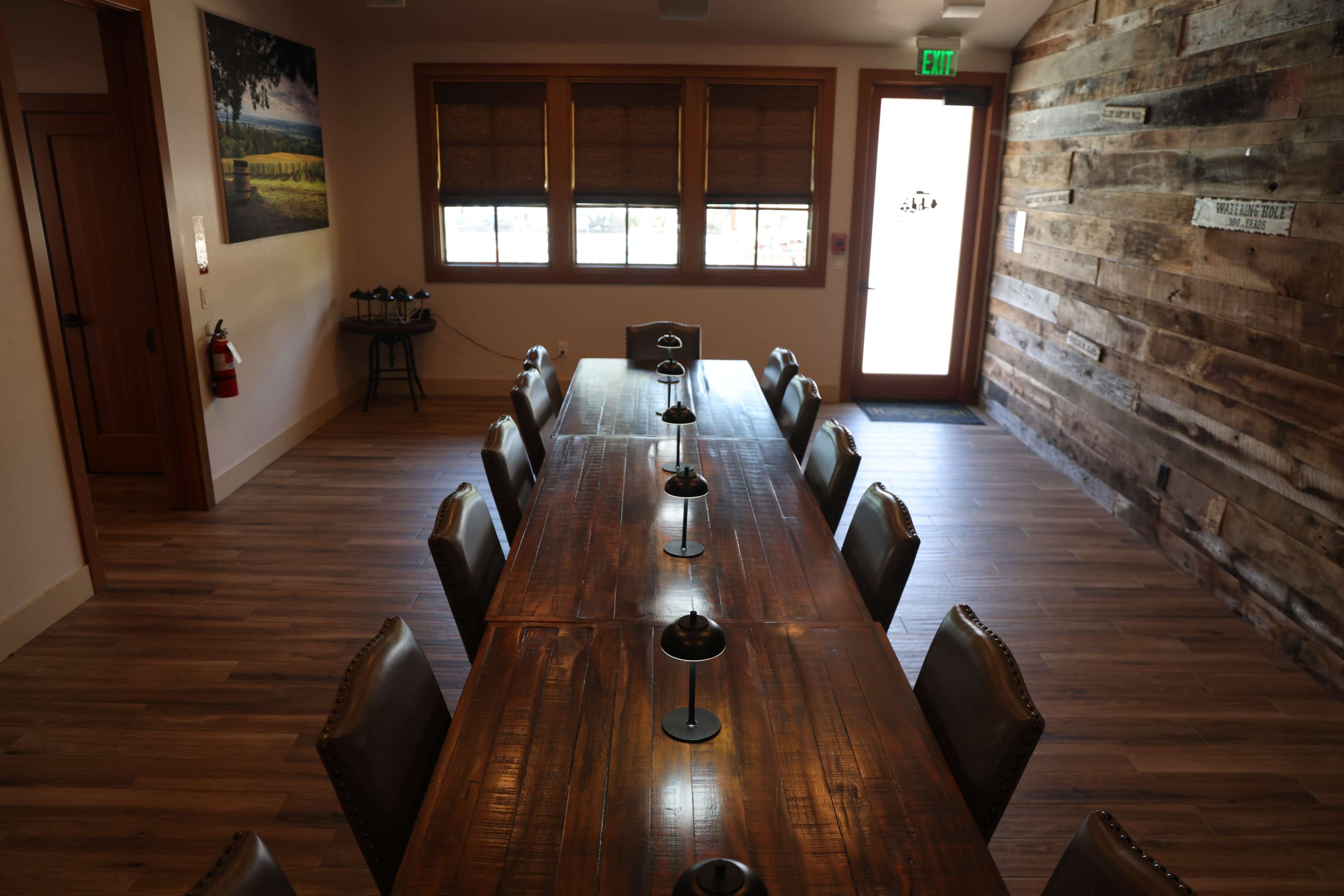 The image shows a large wooden table set in a meeting room with chairs arranged along both sides and a doorway leading outside.