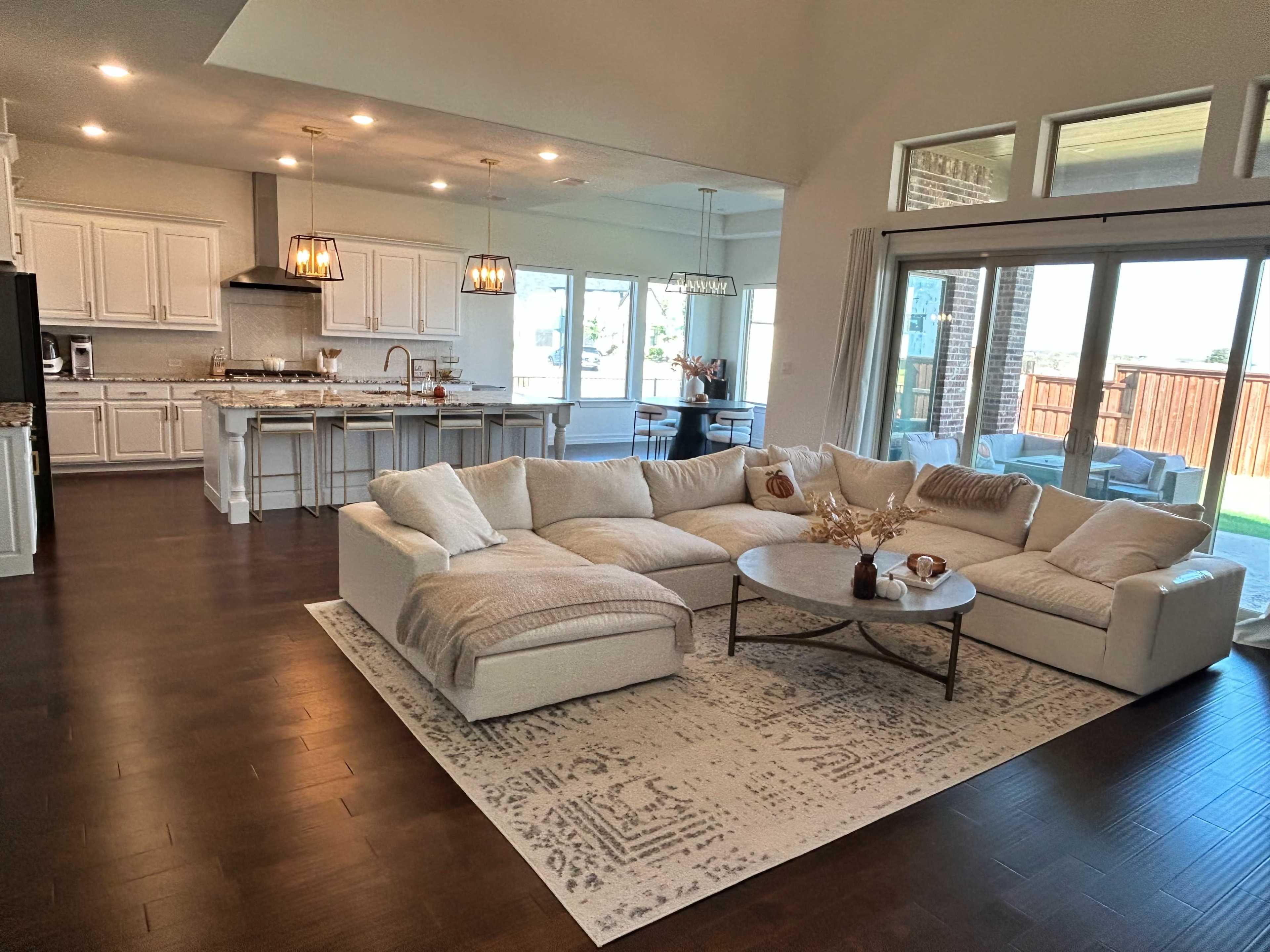 A spacious living room features a large sectional sofa, a central coffee table, and an open layout connecting to a modern kitchen.