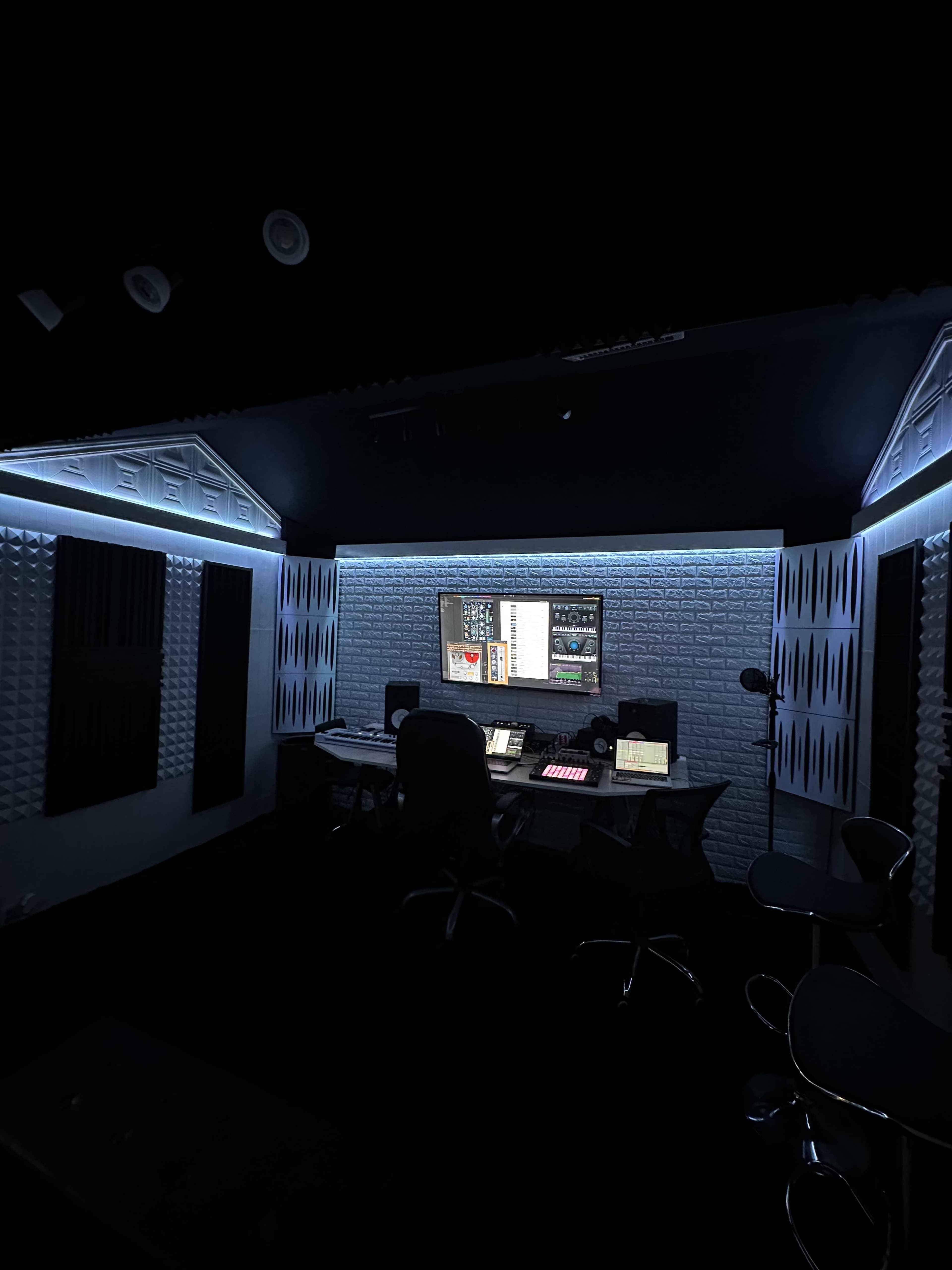 A dimly lit recording studio features a large desk with audio equipment, surrounded by soundproof wall panels.