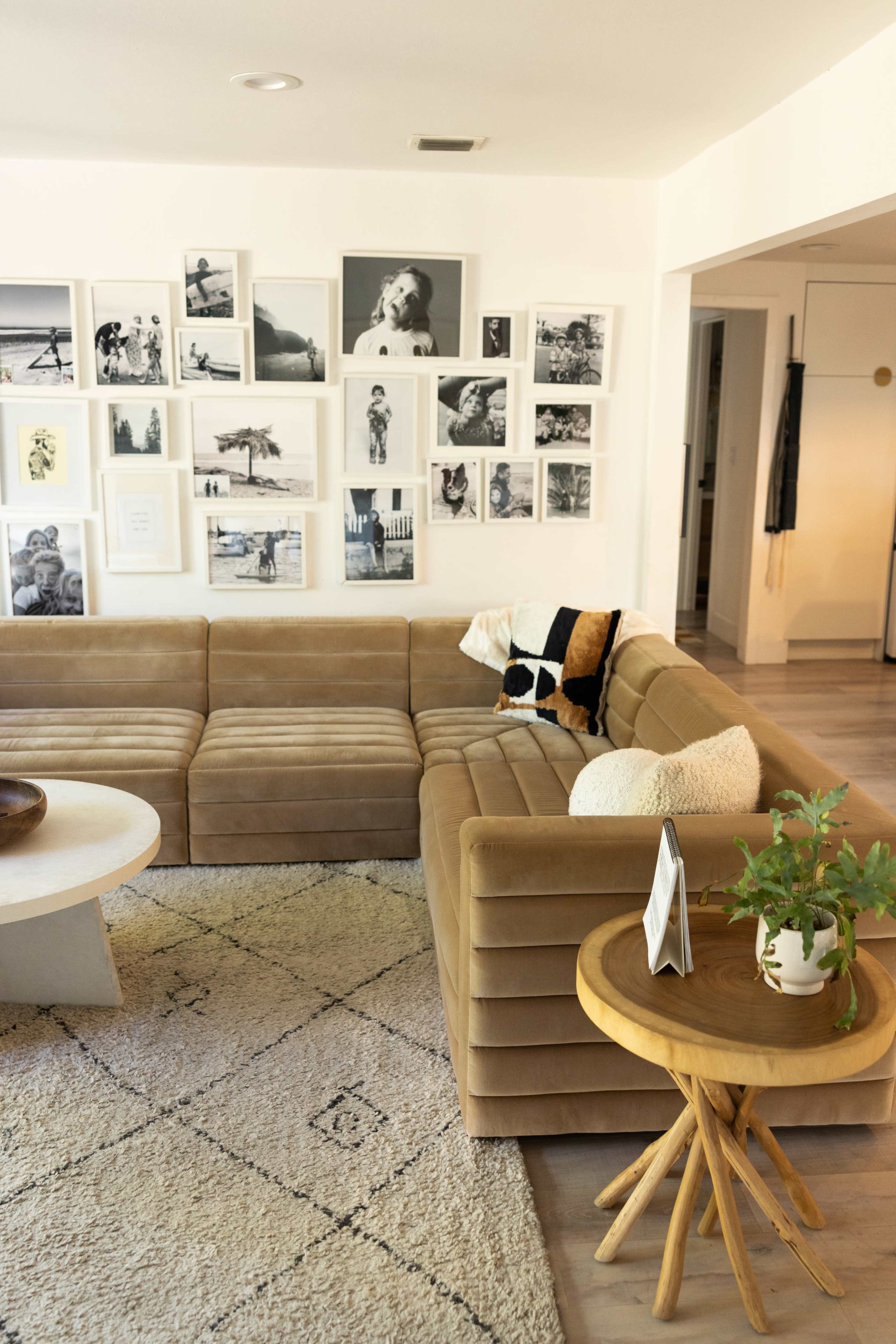 A cozy living room features a beige sectional sofa, a round coffee table, and a gallery wall filled with black-and-white photographs.