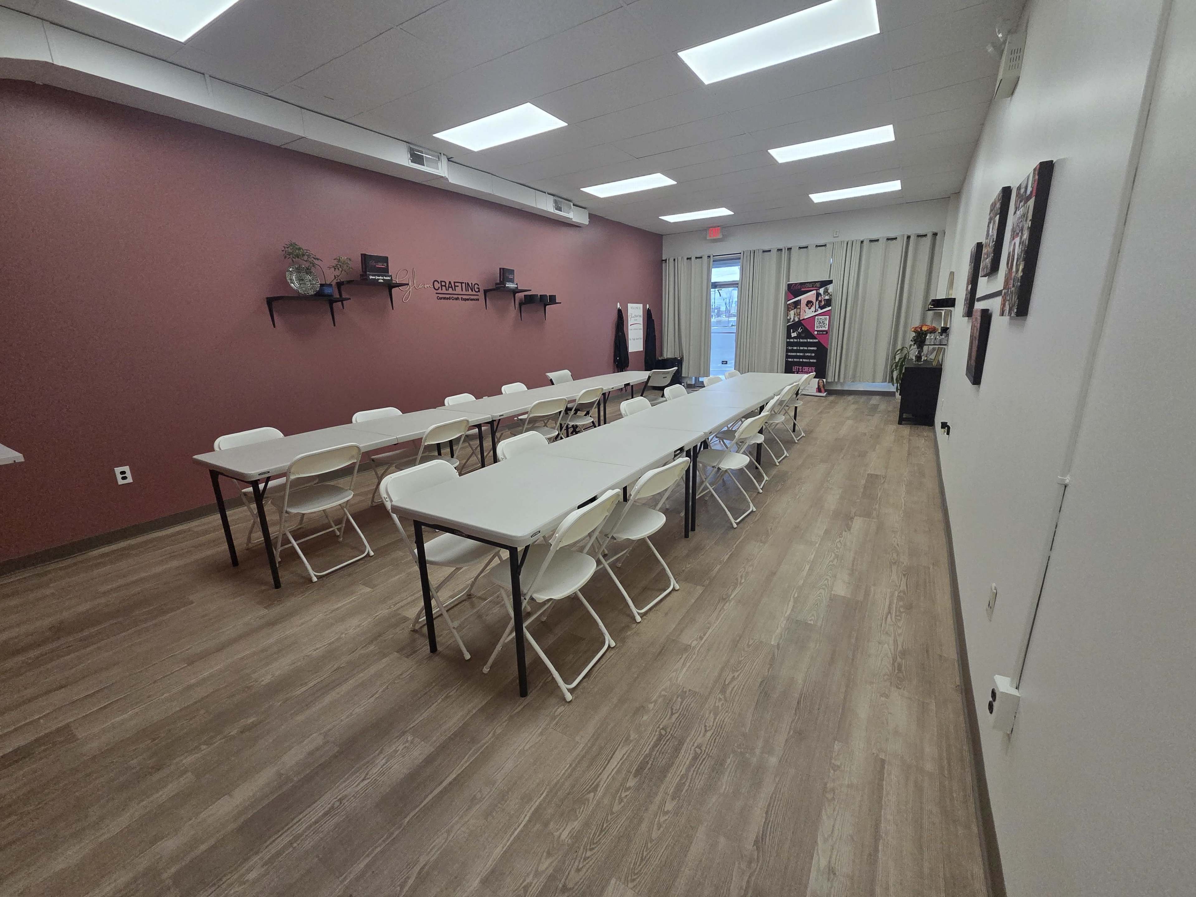 The image shows a spacious meeting room with multiple rectangular tables arranged in parallel, surrounded by white folding chairs, and a dark red accent wall.