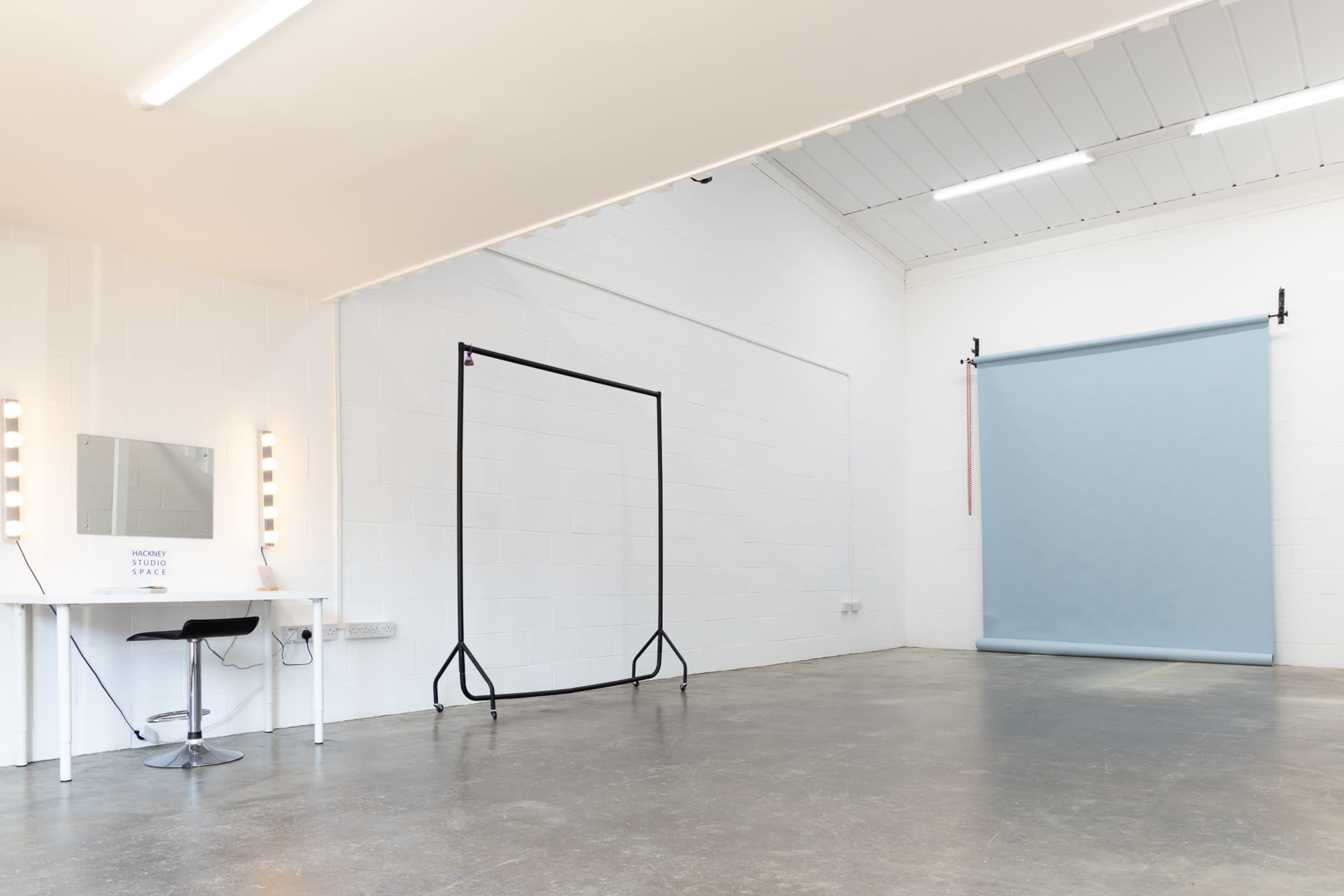 A minimalist studio space with a vanity mirror, a black backdrop stand, and a light blue backdrop attached to the wall.