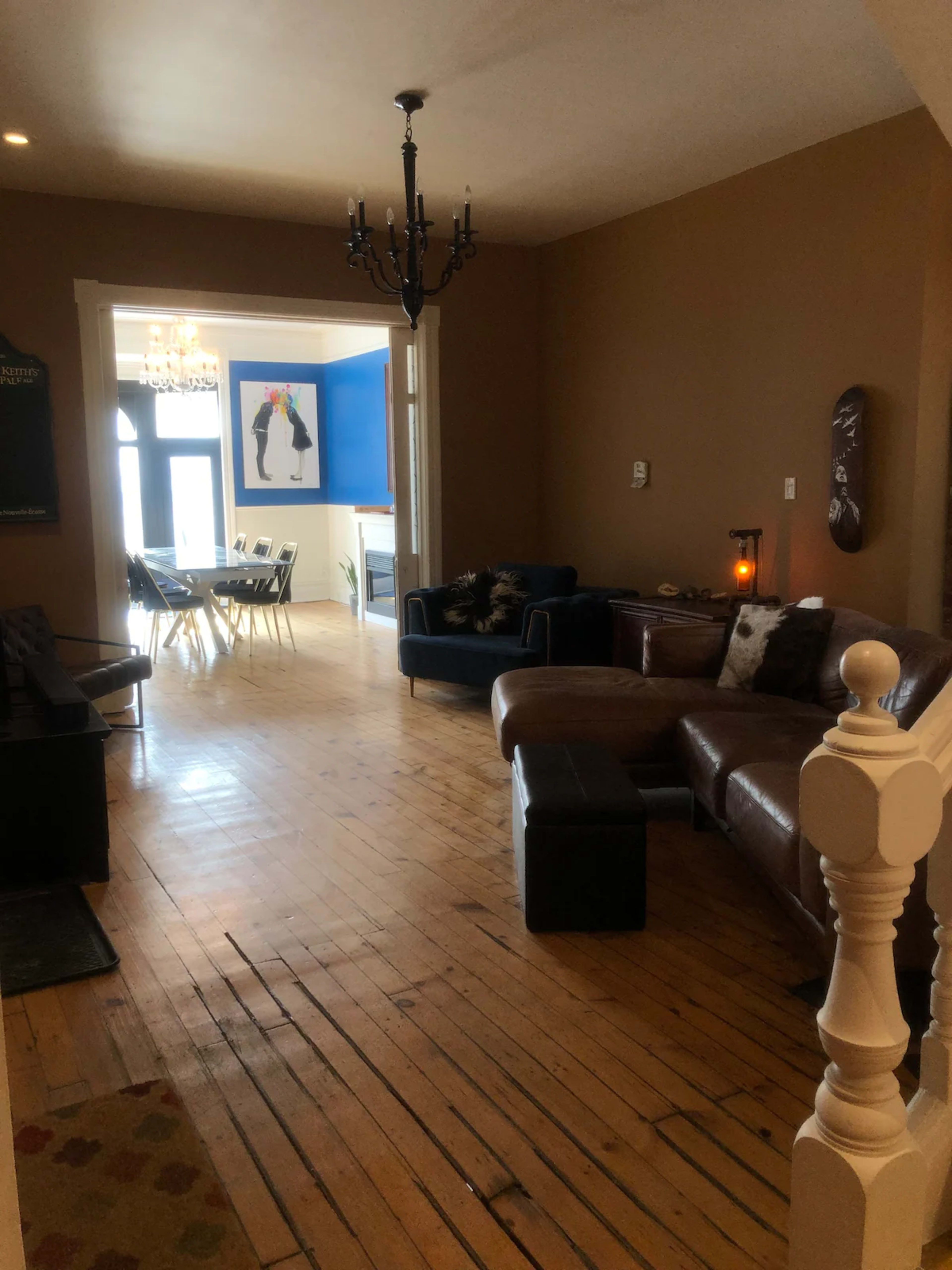 The image shows a hallway leading to a dining area, featuring wooden floors, a brown-painted wall, and a seating arrangement with a couch and chairs.