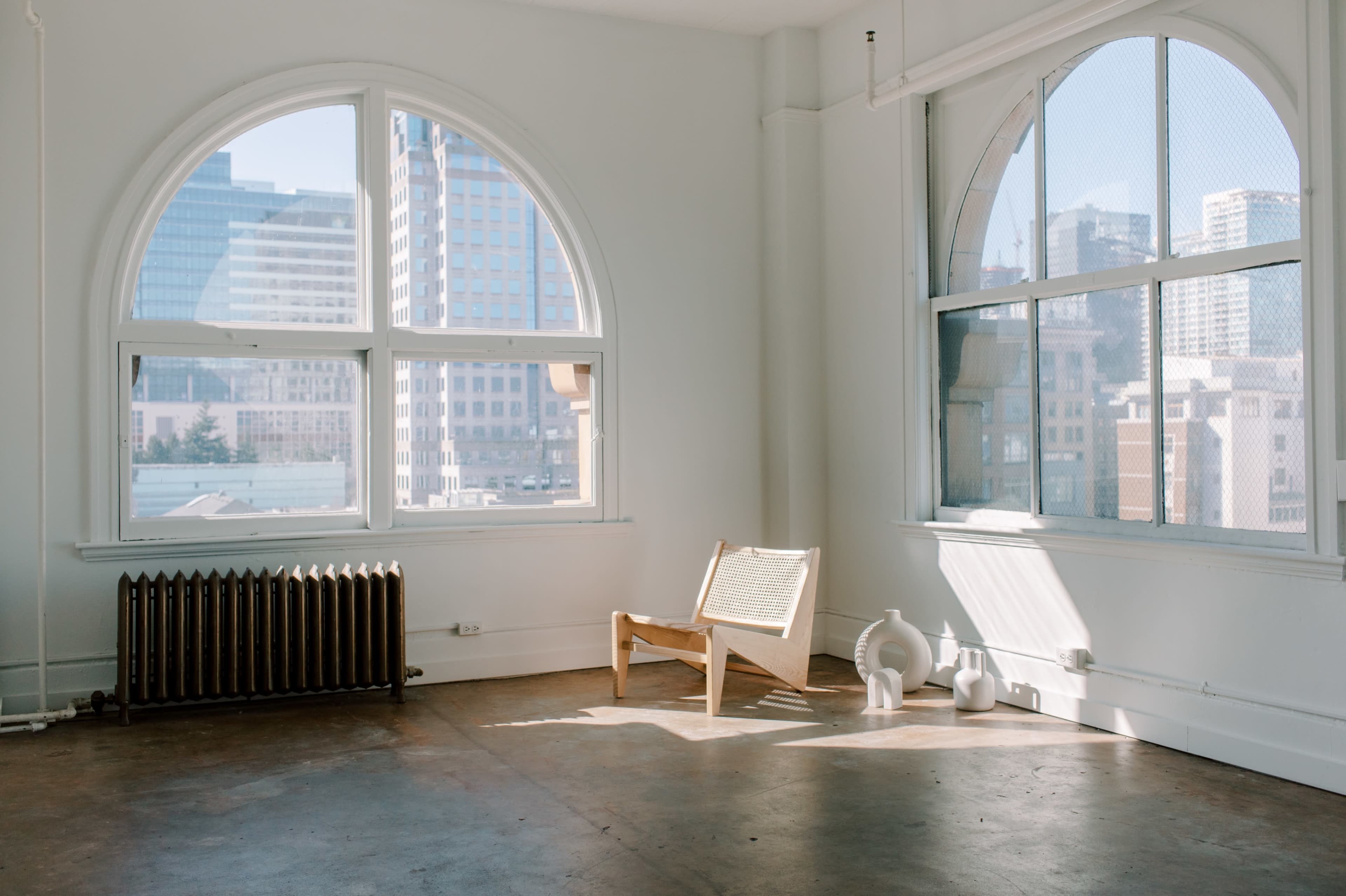 A minimalist room with large arched windows, a wooden chair, and a couple of decorative white vases.