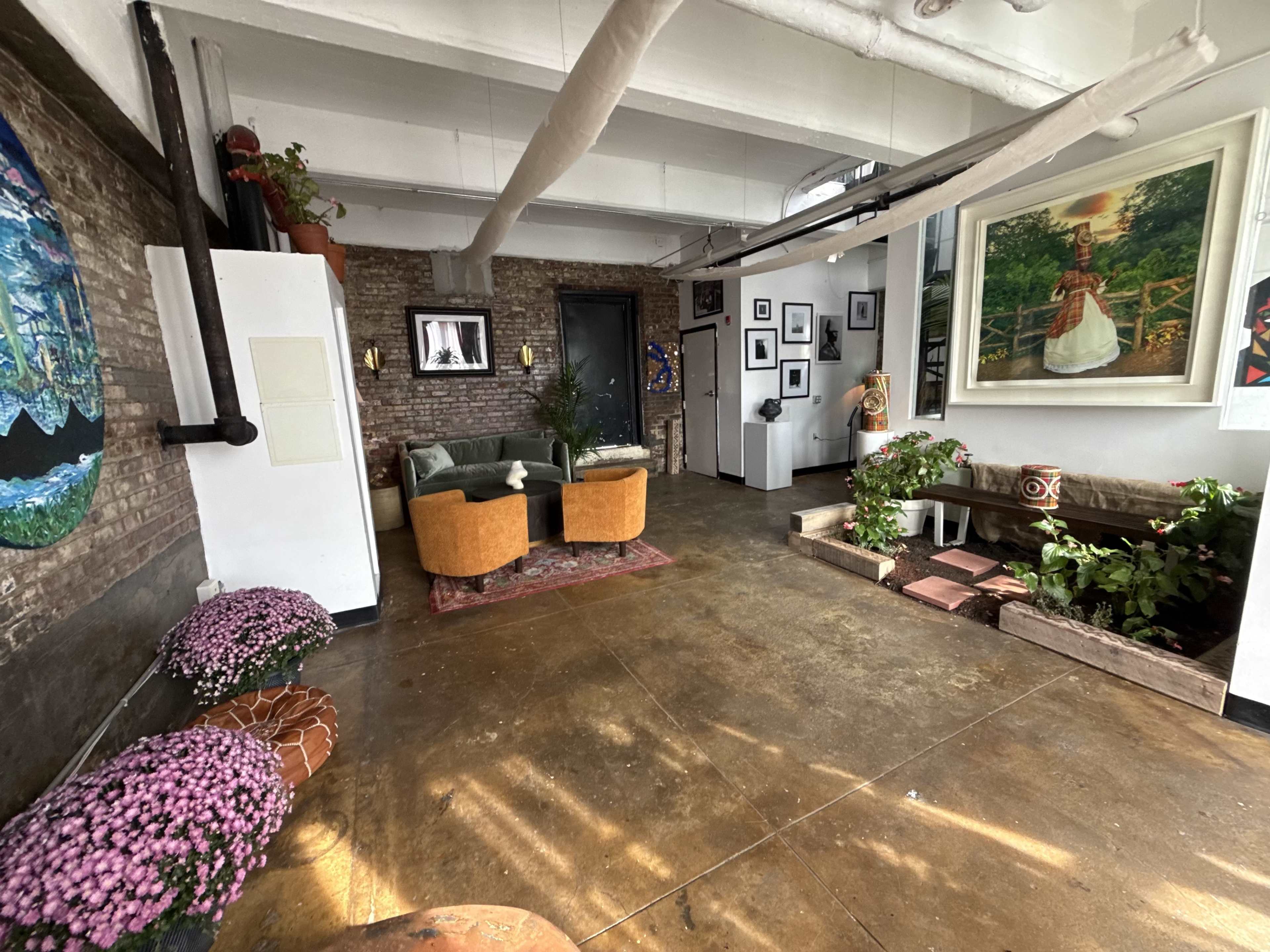 The image shows a spacious room with exposed brick walls, modern furniture, and various artworks displayed on the walls.