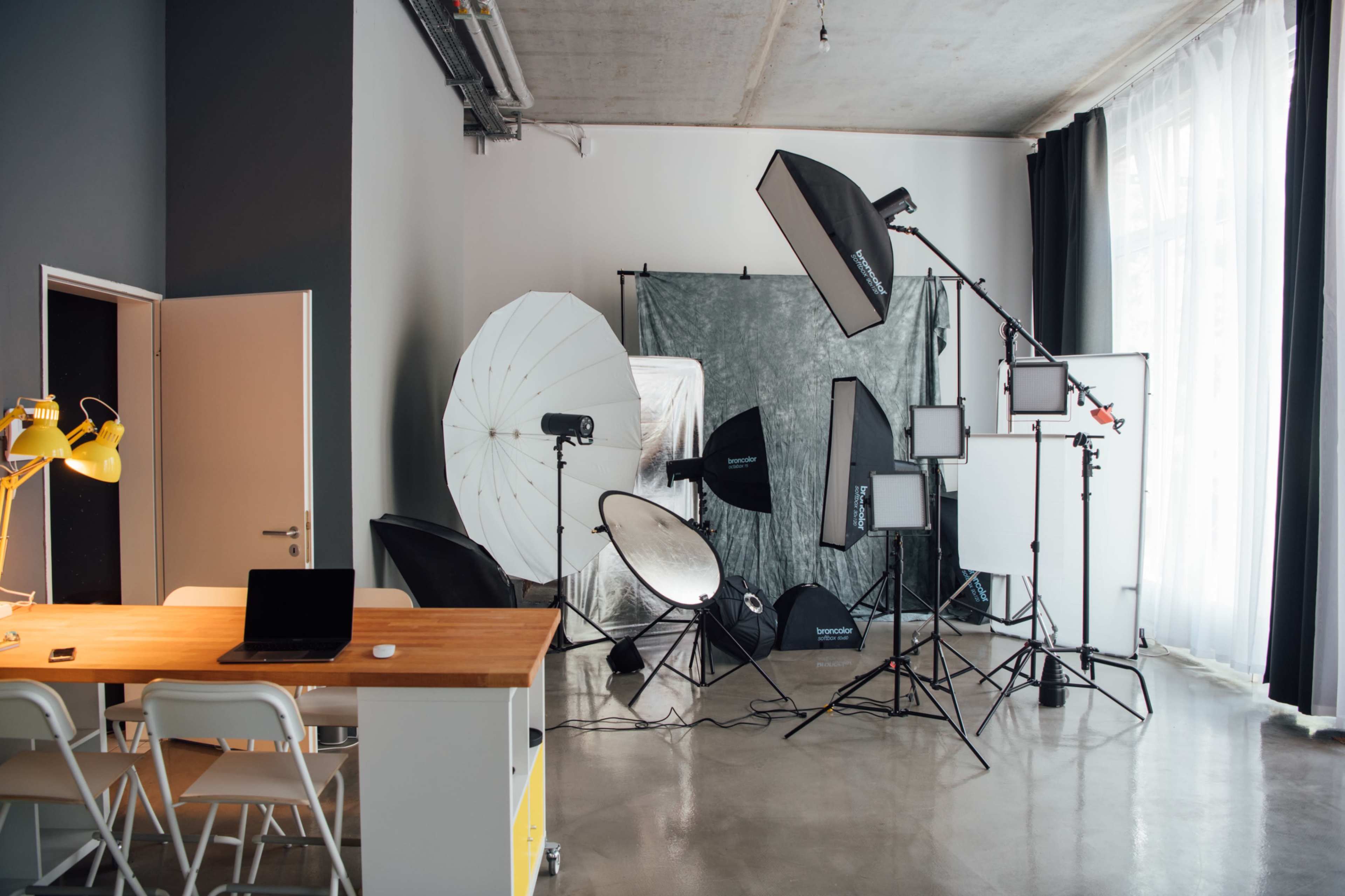 A photography studio is equipped with various lighting setups, including softboxes and reflectors, alongside a wooden table and chairs.