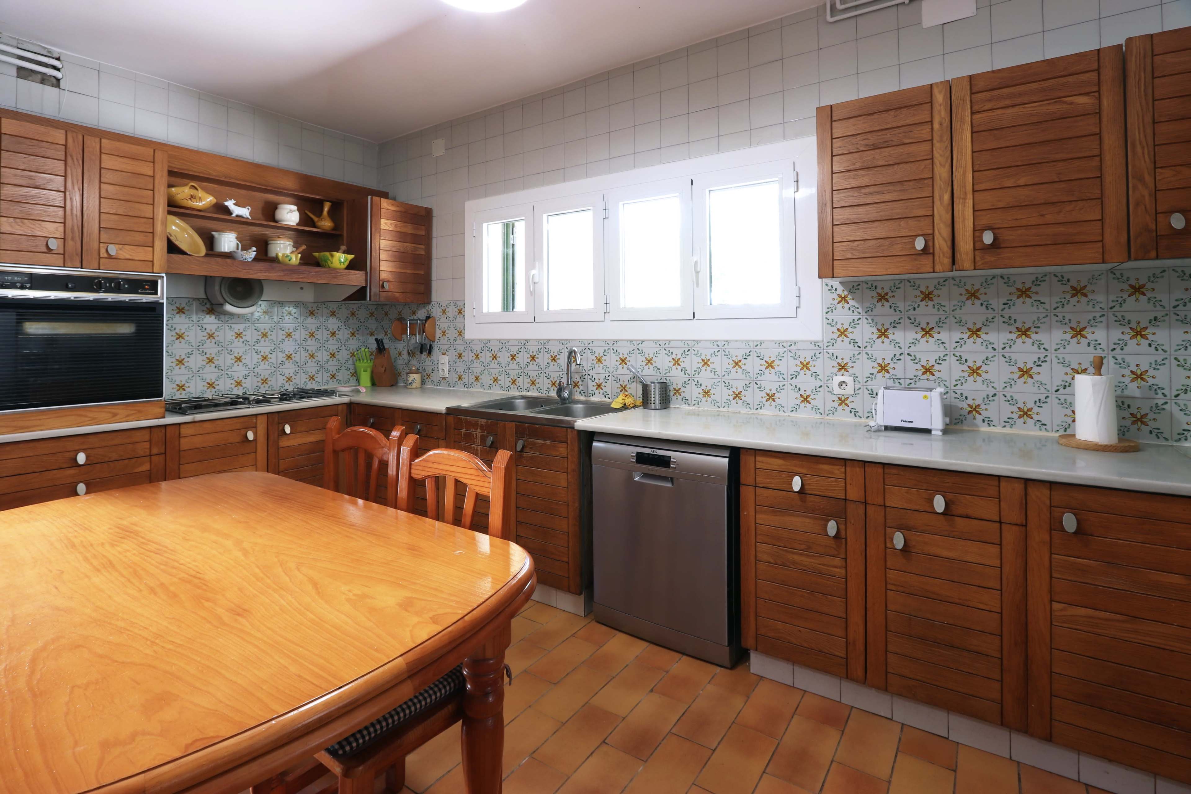The kitchen features wooden cabinets, a marble countertop, and a dining table surrounded by four chairs, with decorative tiles on the walls.
