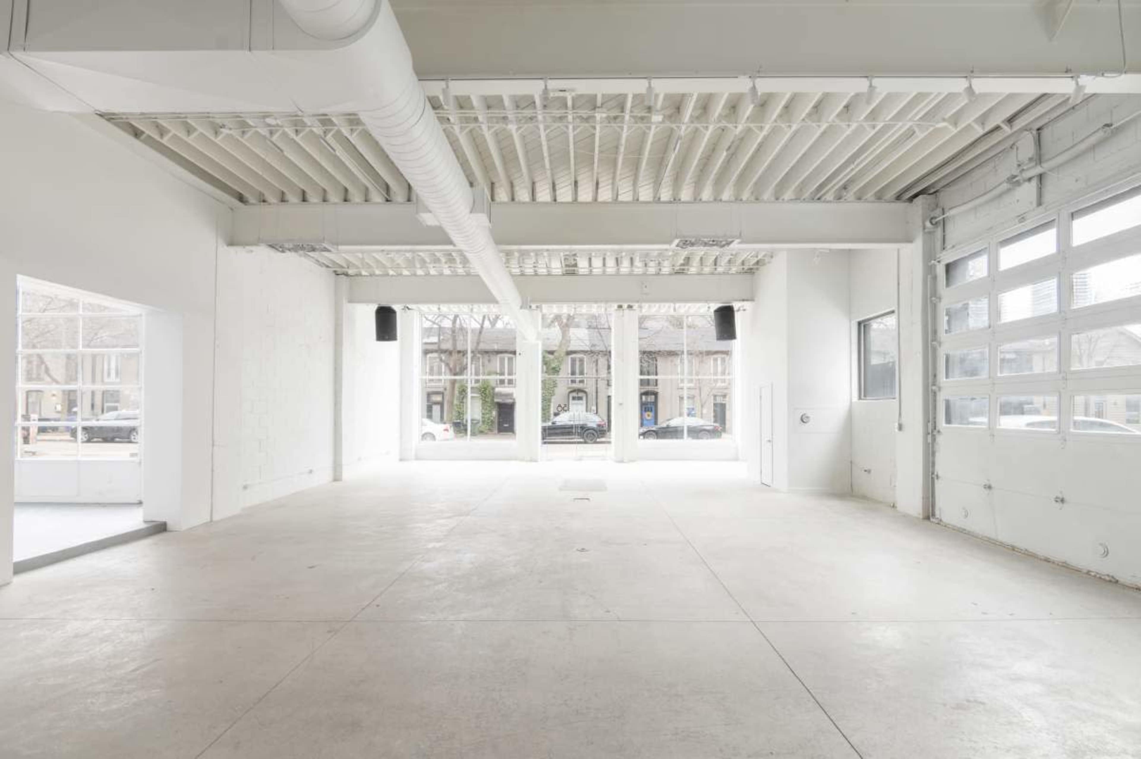 The image shows a spacious, empty interior with high ceilings, large windows, and concrete flooring.