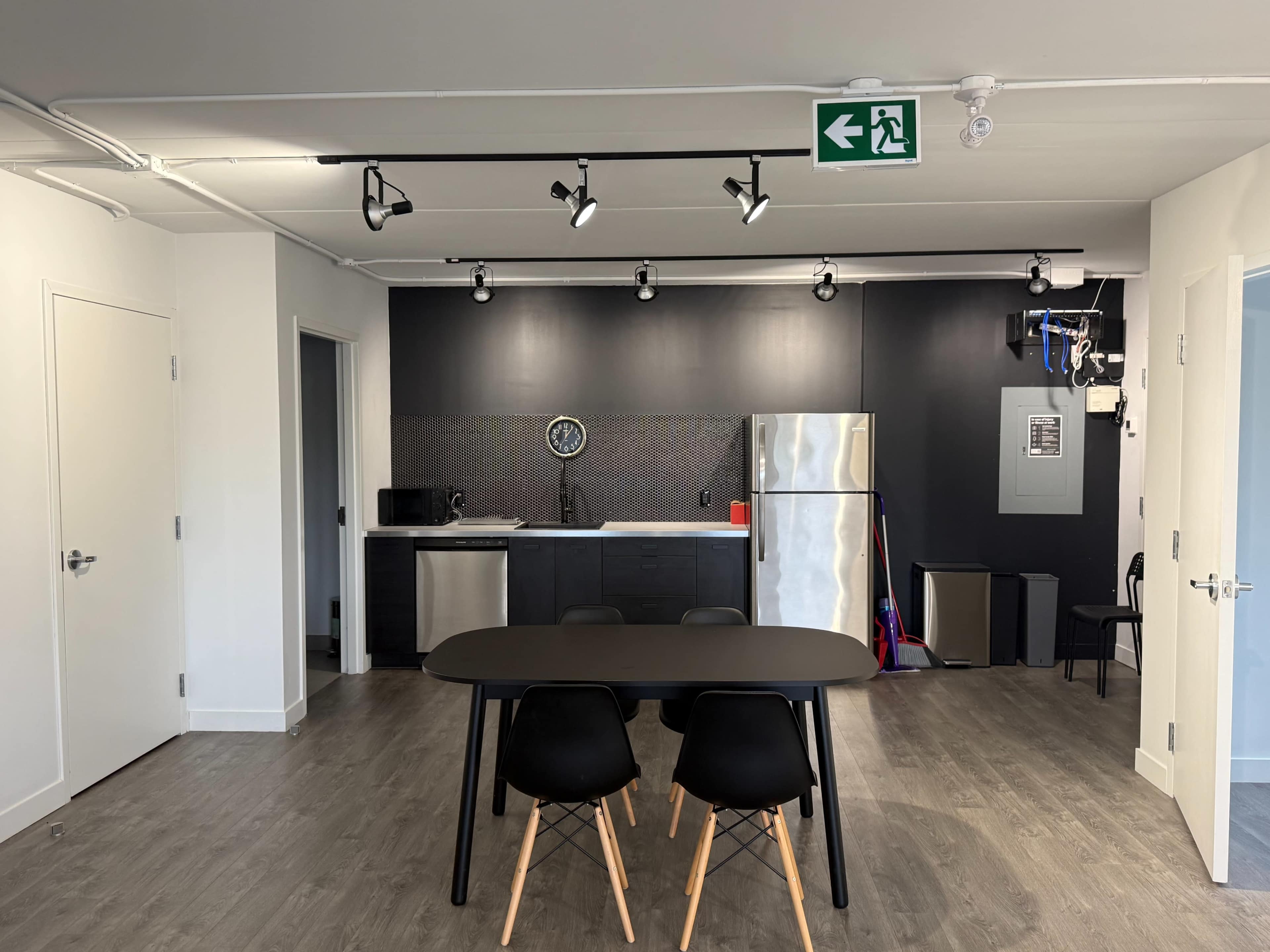 The image shows a modern kitchen and dining area featuring a black and silver color scheme, with a dining table and four chairs in the foreground.
