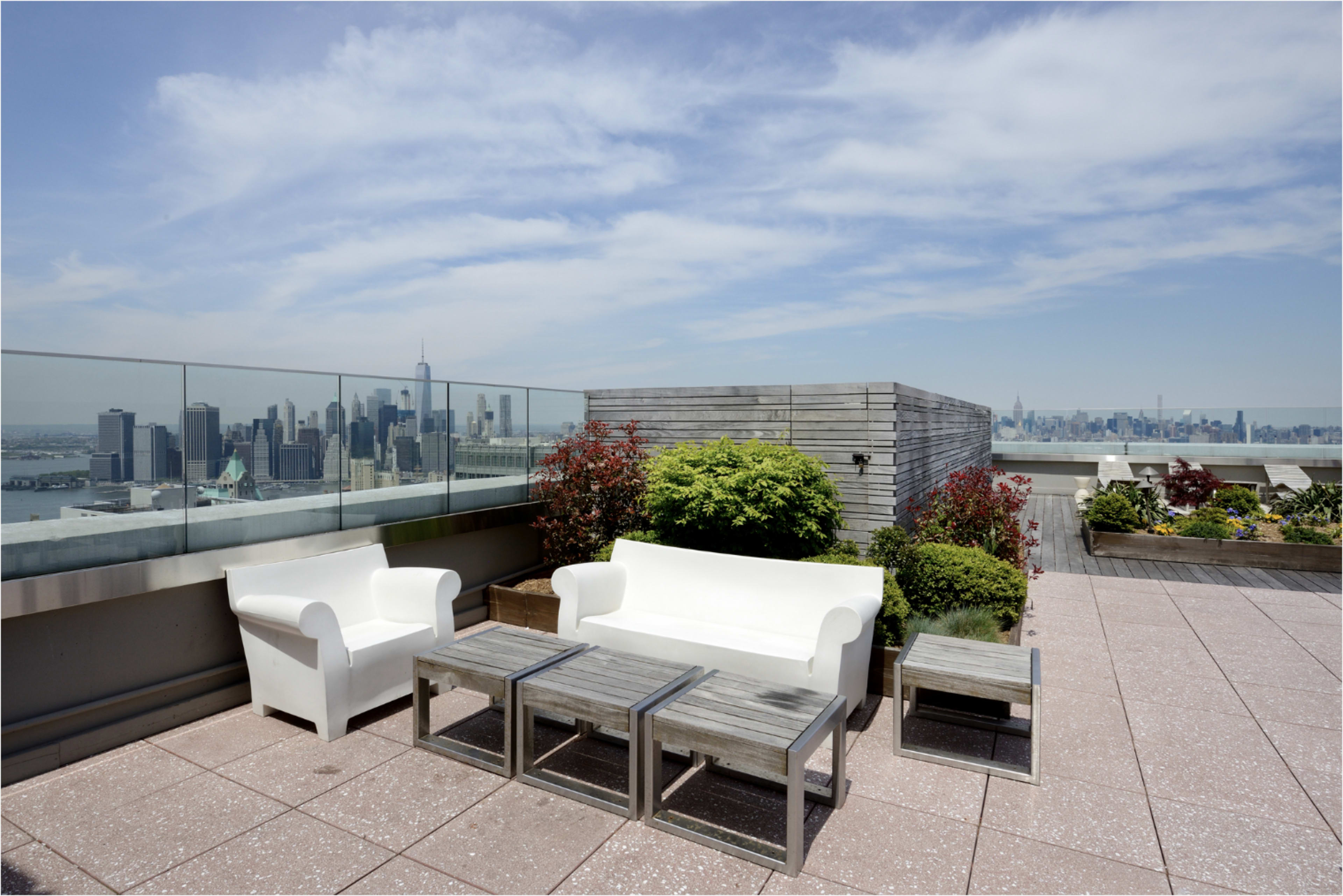 The rooftop terrace features white outdoor seating and wooden tables with a view of a city skyline in the background.