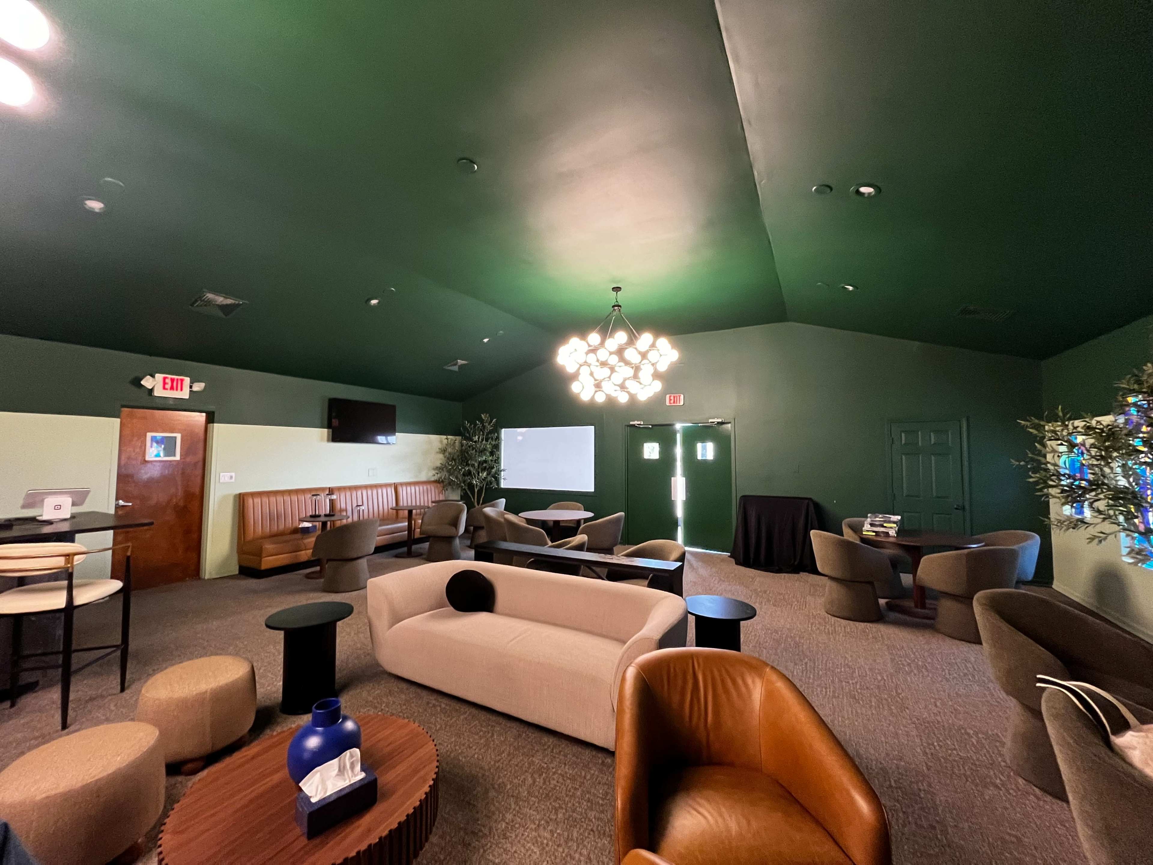 The room features a green ceiling and walls, with various seating areas including couches, tables, and a chandelier hanging overhead.