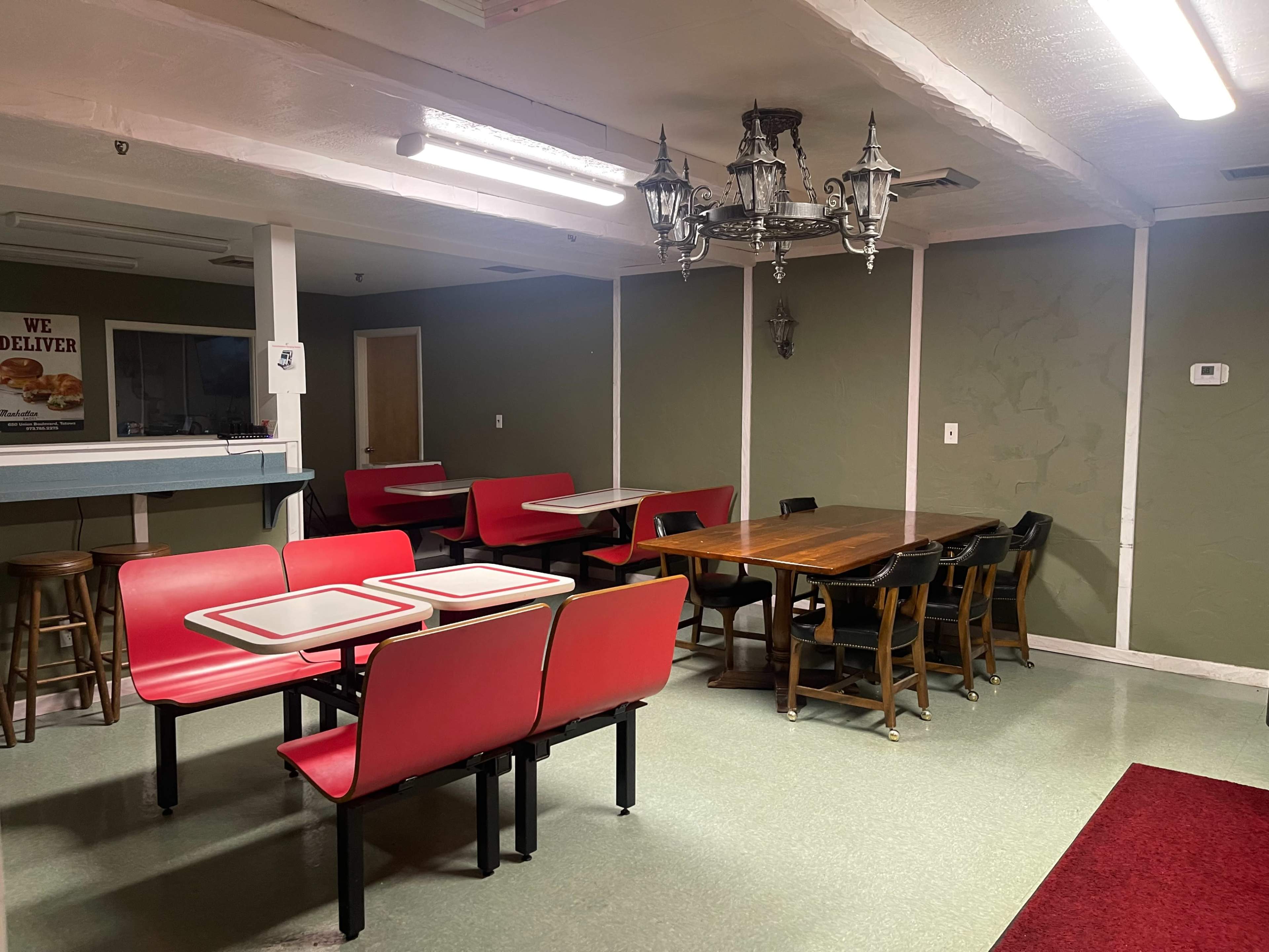 The image shows a dining area with several tables and chairs, including red and black seating, under a chandelier, along with a serving counter in the background.