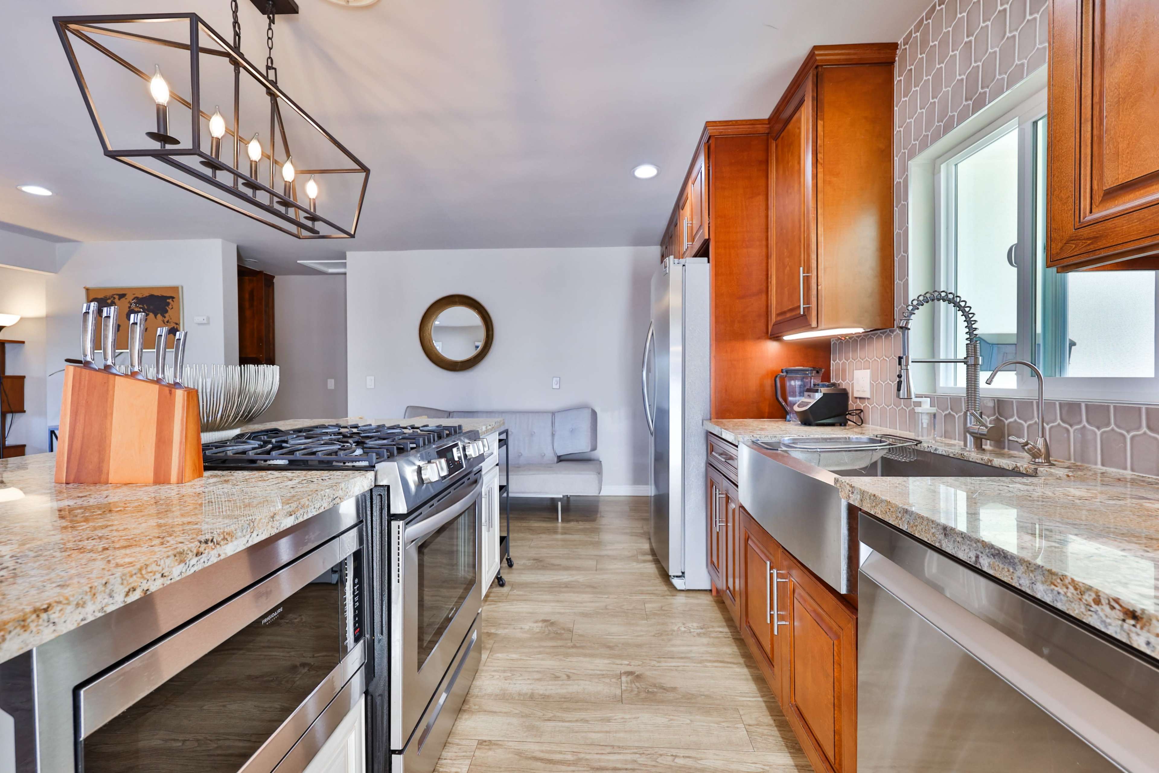 A modern kitchen featuring wooden cabinets, granite countertops, stainless steel appliances, and a gas stove with a stylish light fixture above.