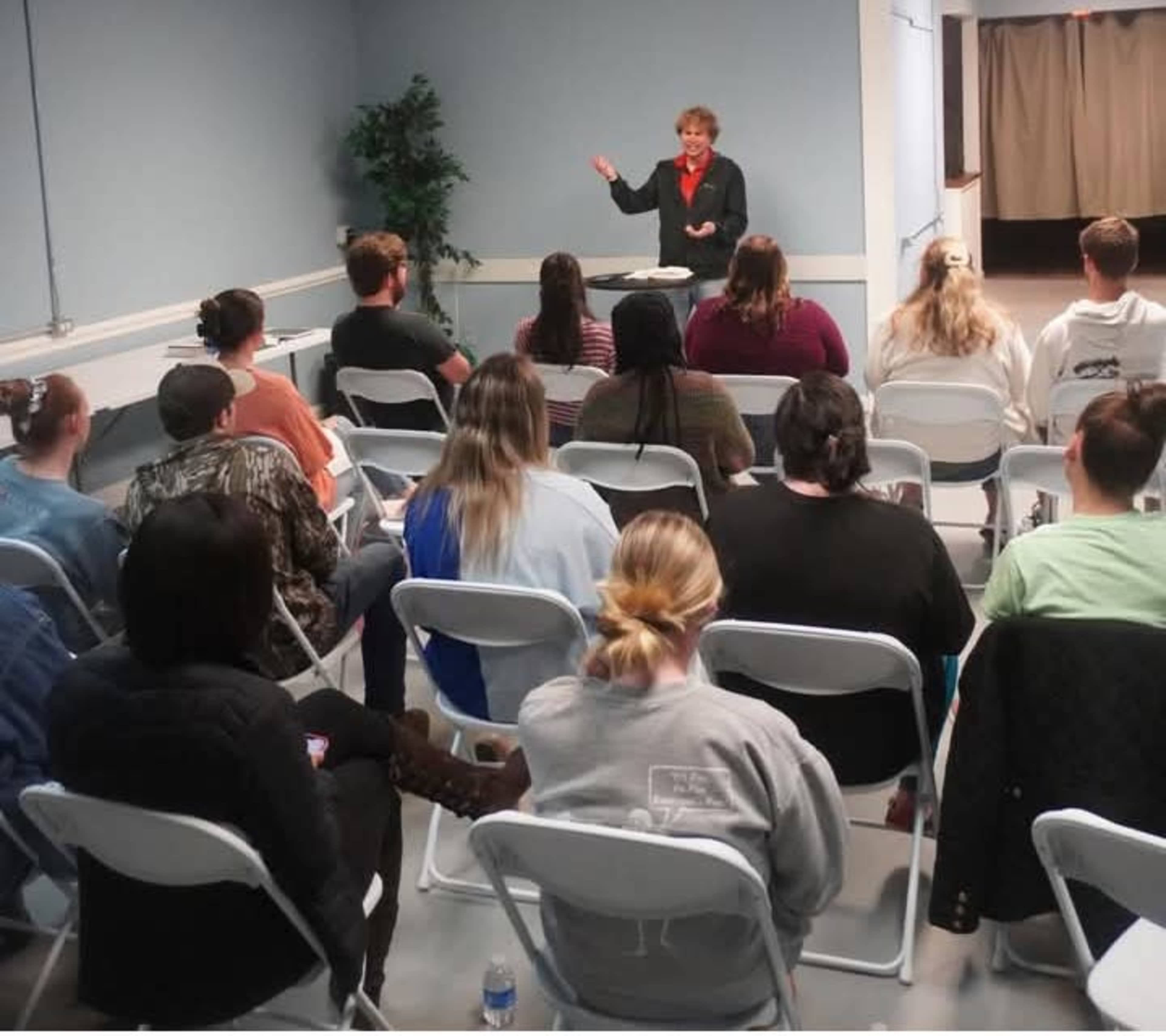 A speaker stands in front of a seated audience in a meeting room.