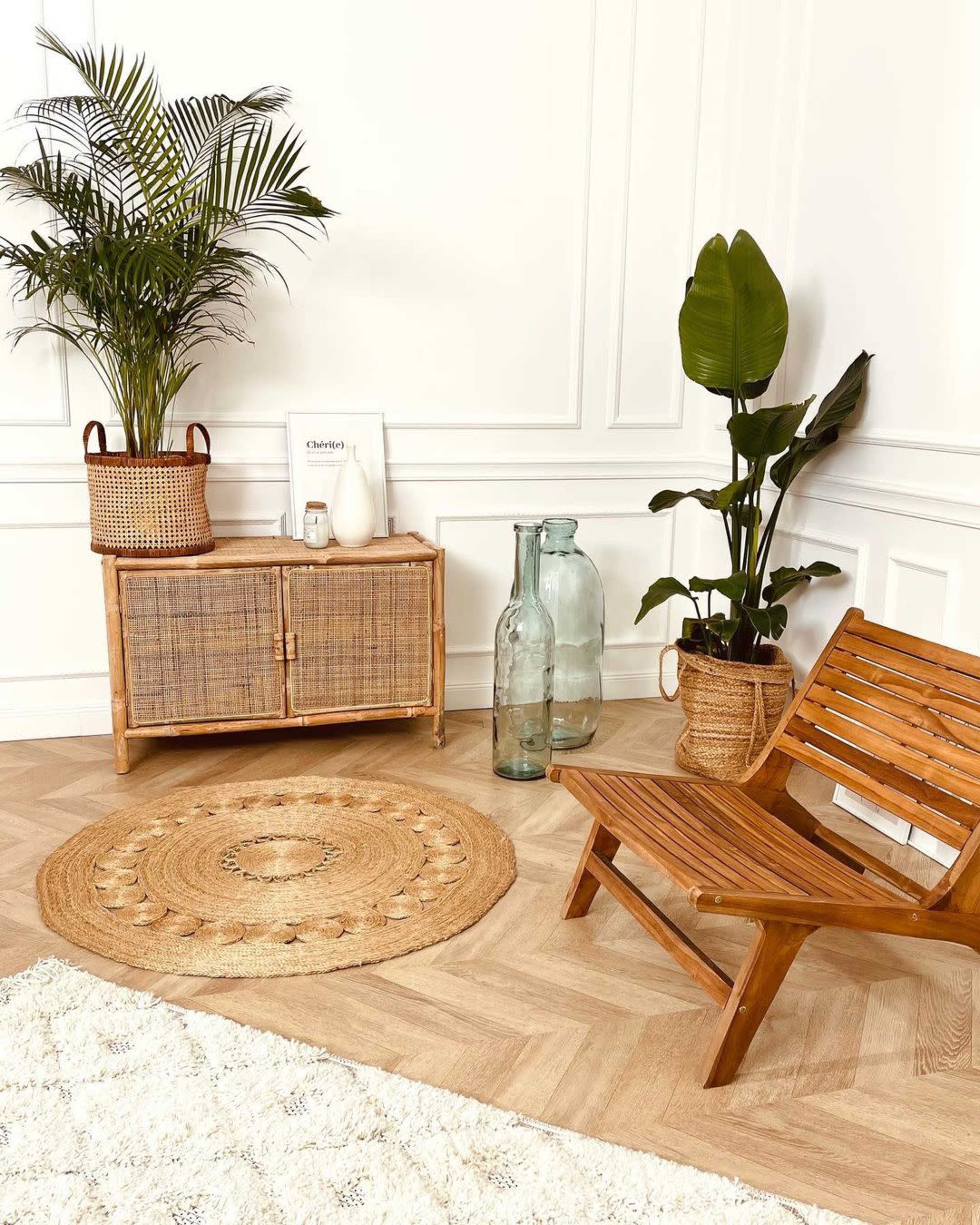 A cozy corner featuring a wooden chair, a rattan cabinet, potted plants, and decorative bottles on a patterned rug.