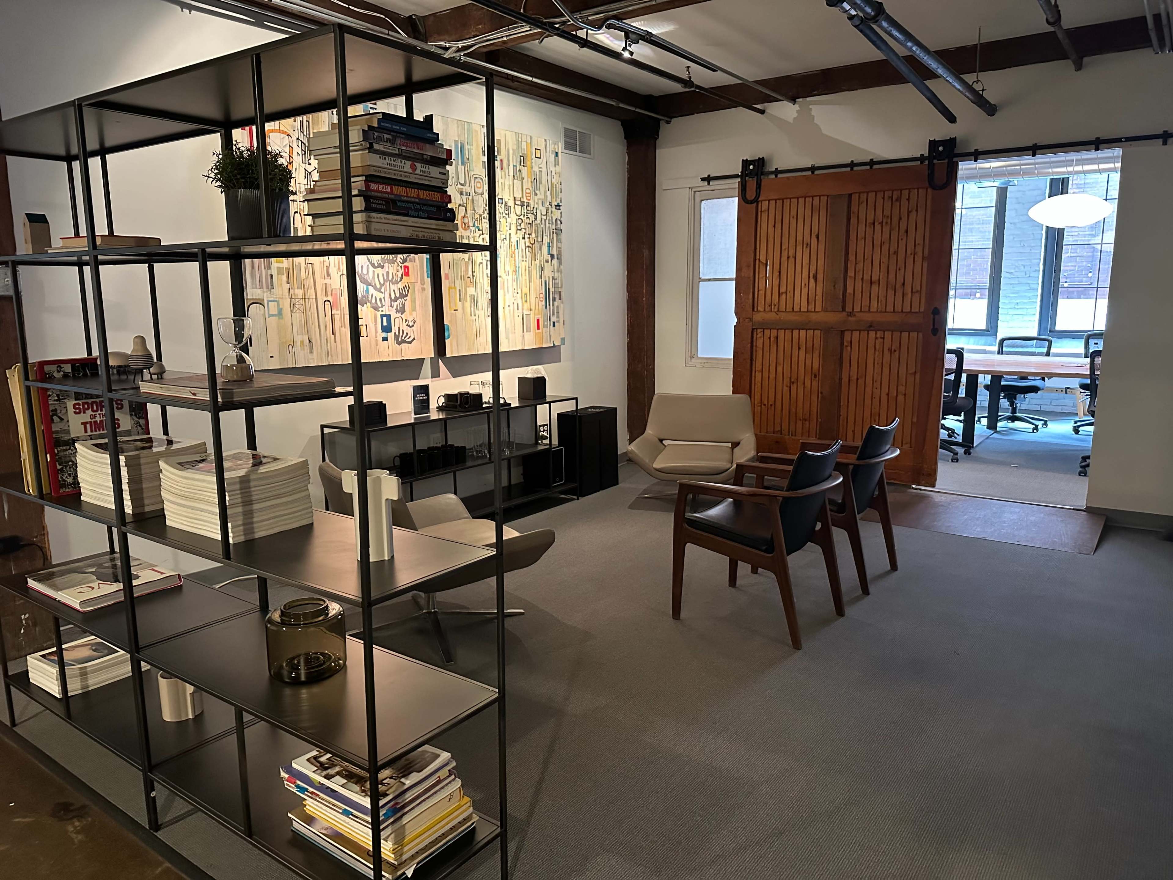 A modern office space with a bookshelf, art on the wall, seating area, and a sliding wooden door leading to a conference room.