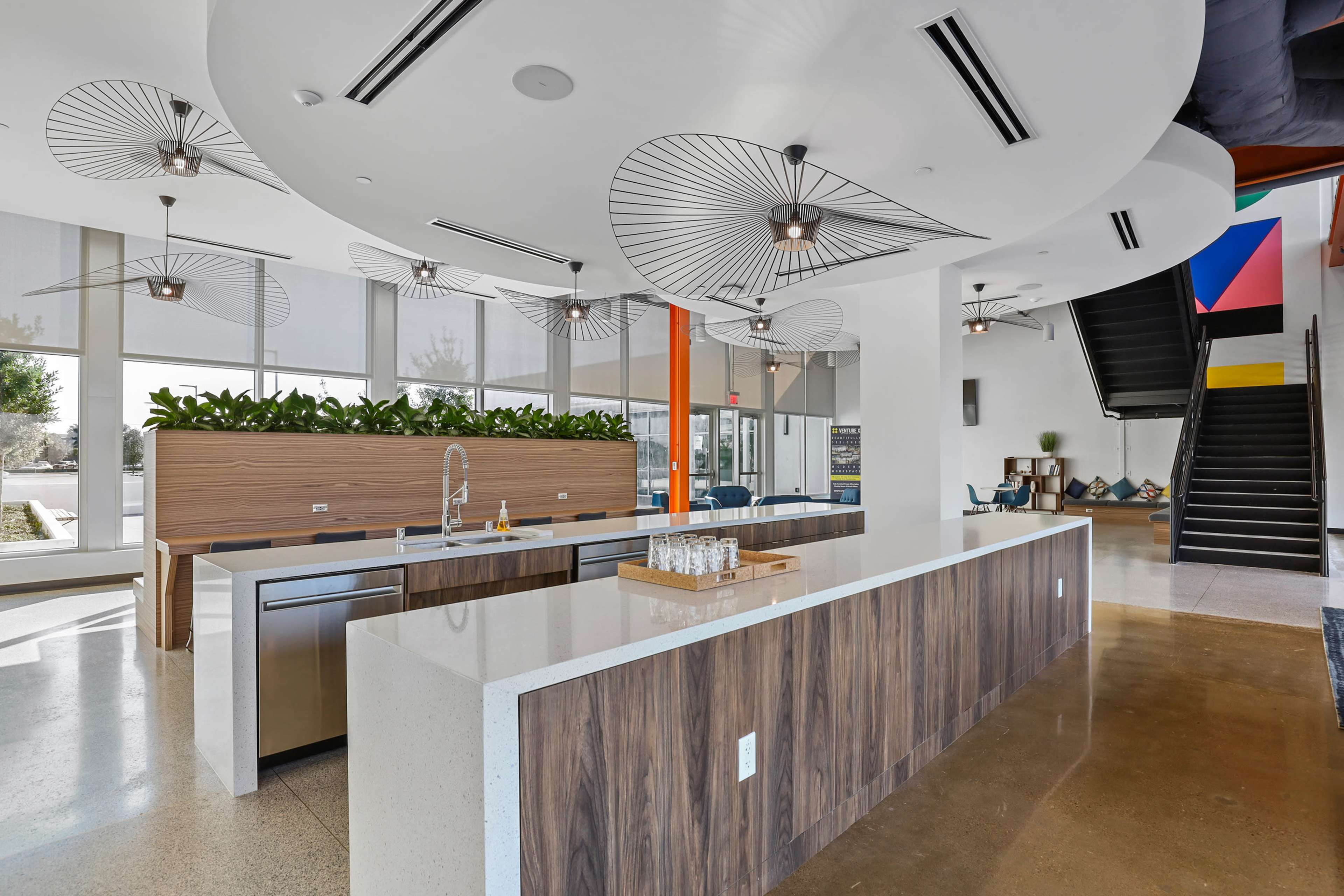 A modern open-plan kitchen area with a large island, stainless steel appliances, and unique fan lighting fixtures.