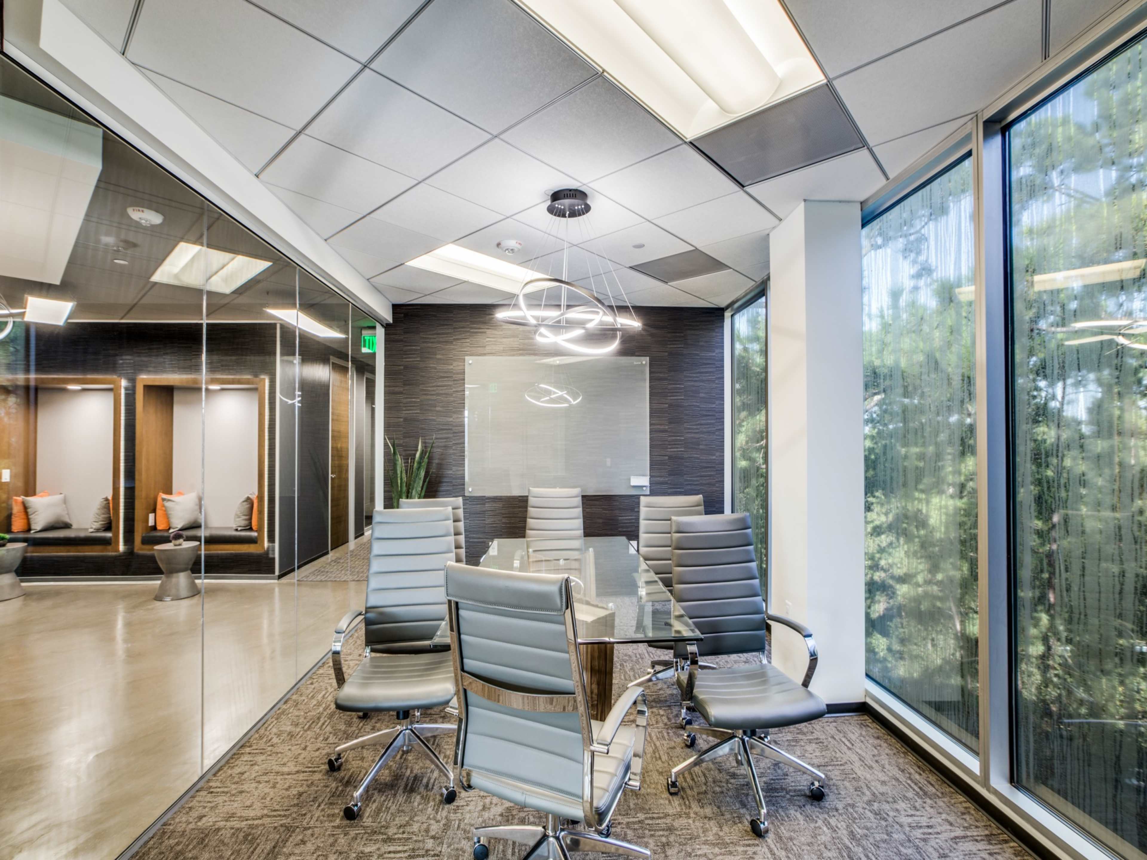 A modern conference room features a glass table surrounded by ergonomic chairs, with large windows providing a view of the outdoors.