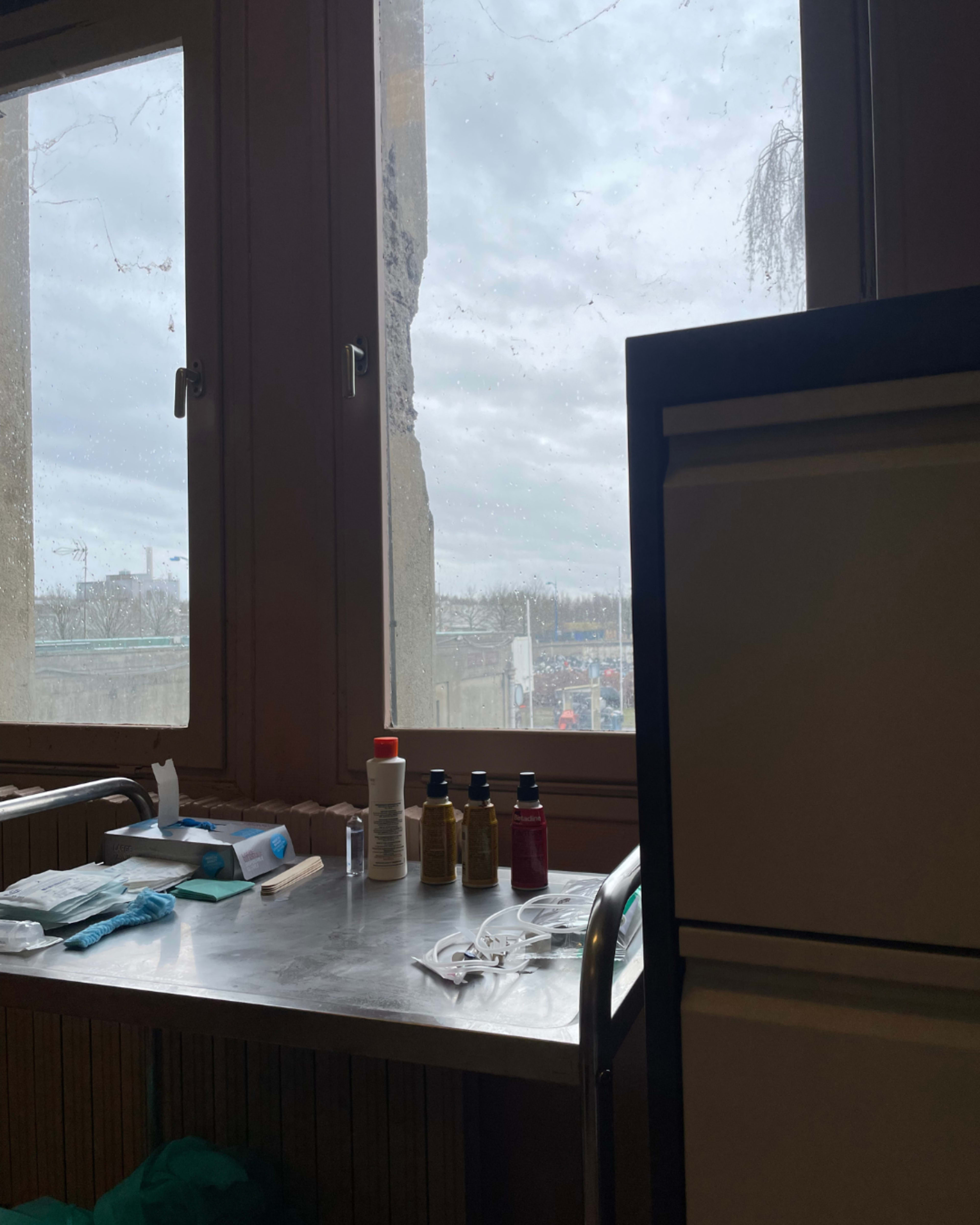A medical workspace is set up with various supplies on a stainless steel table, and a view of a cloudy outdoor scene through a window.