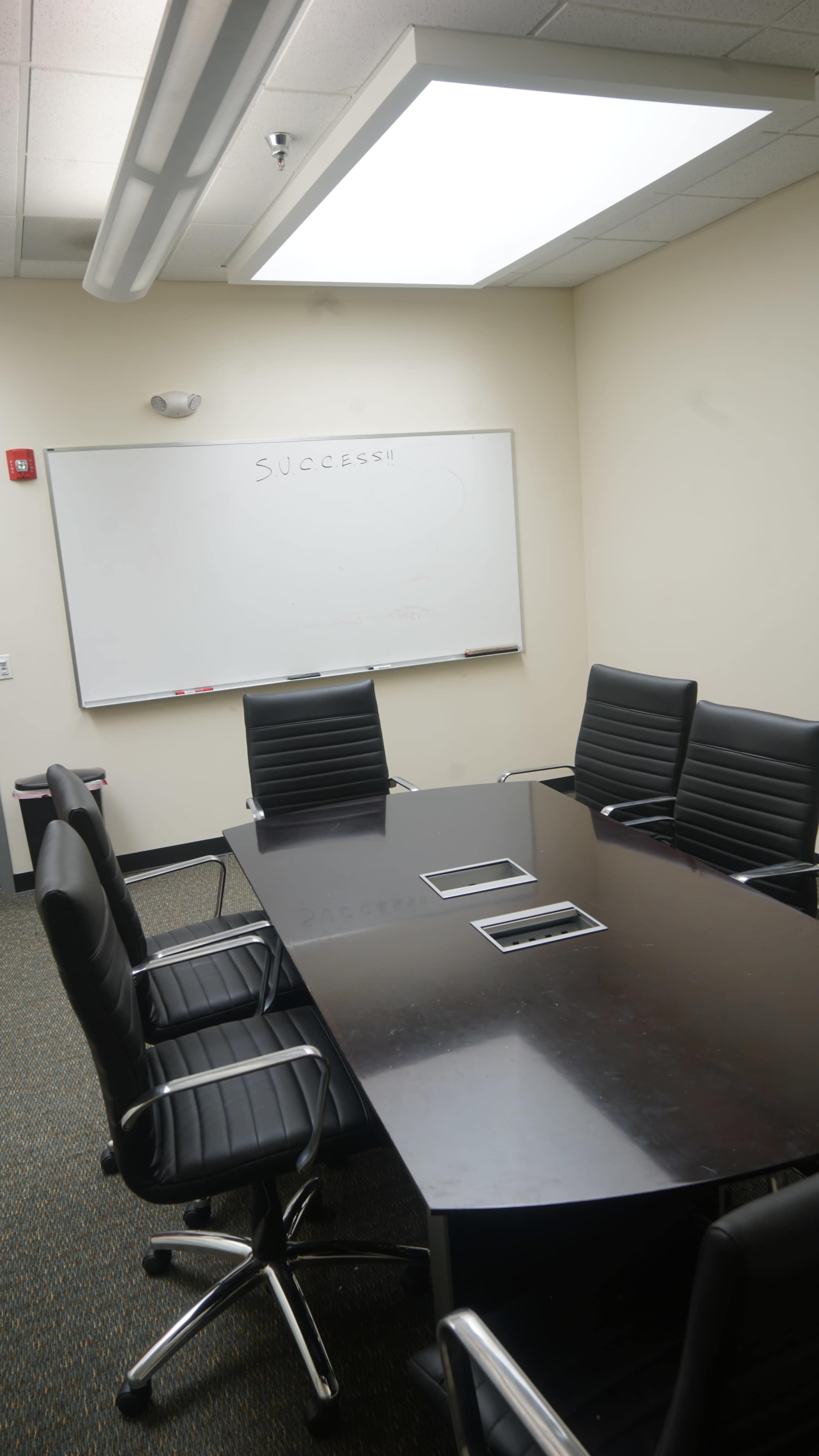 A conference room features a large table surrounded by black chairs and a whiteboard with the word "SUCCESS" written on it.