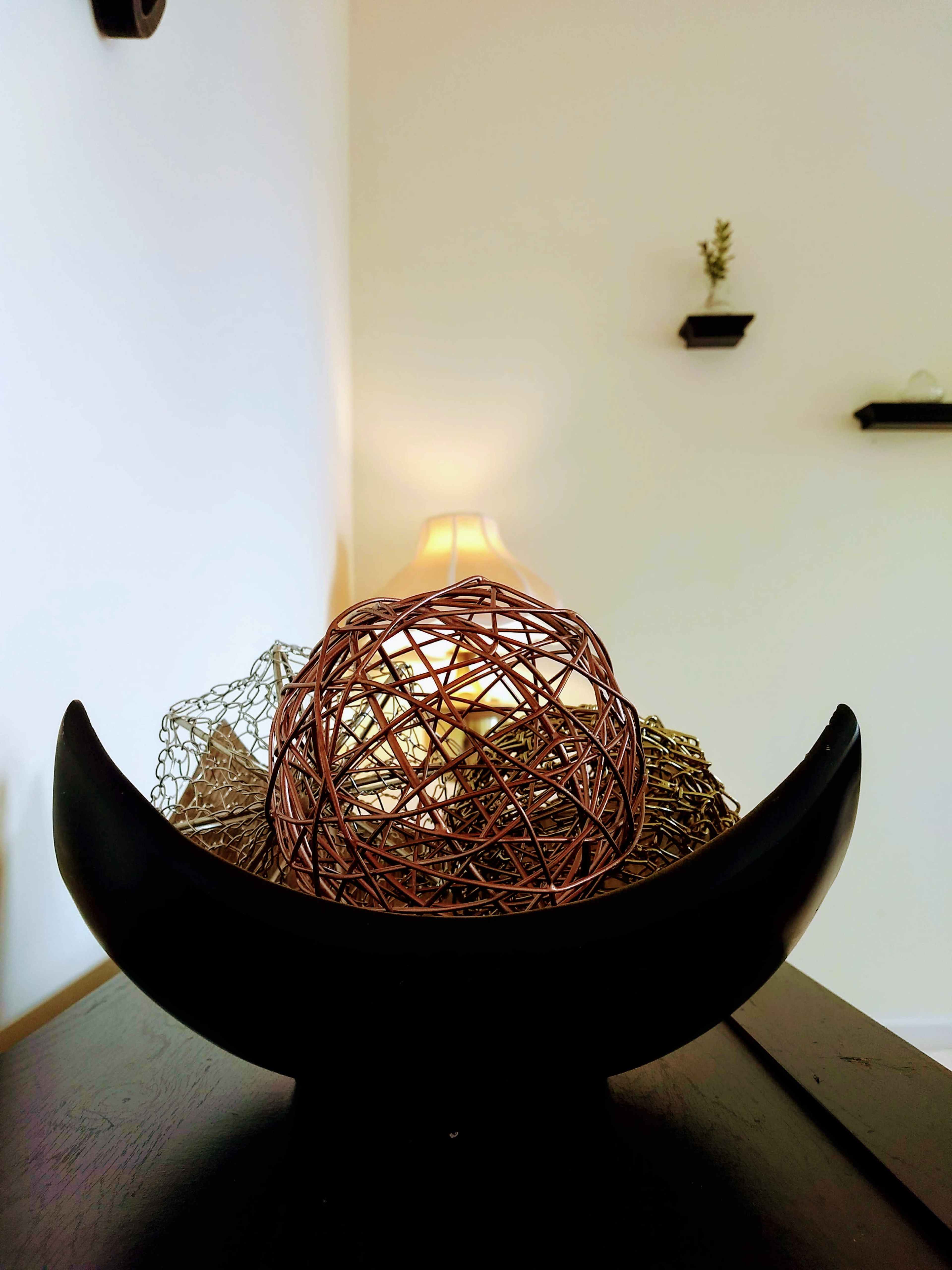A black bowl contains decorative spheres made of wire and string, with a lamp glowing softly in the background.