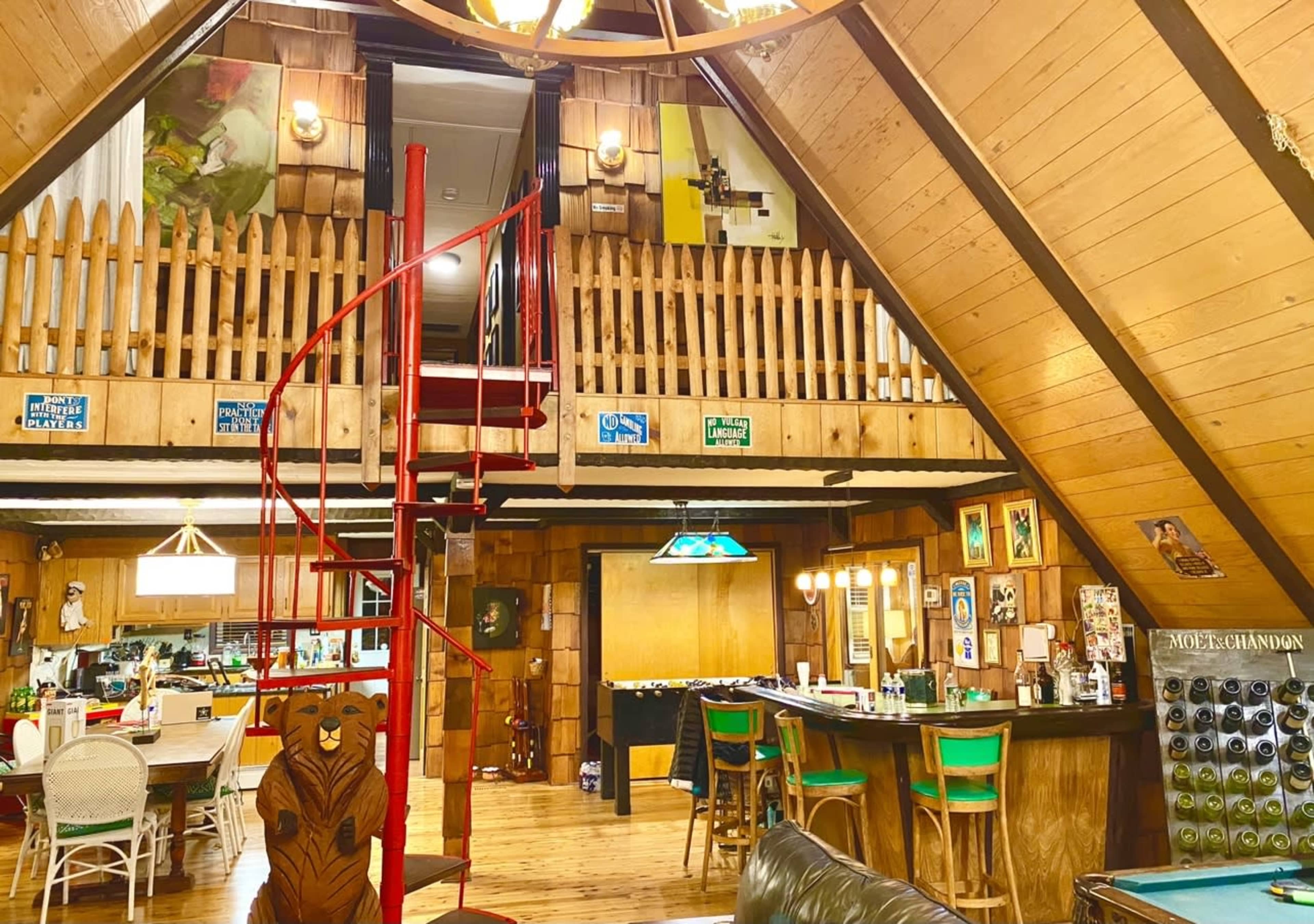 The image shows a rustic A-frame cabin interior featuring a spiral staircase, wooden walls, a bar area, and various decorative items.