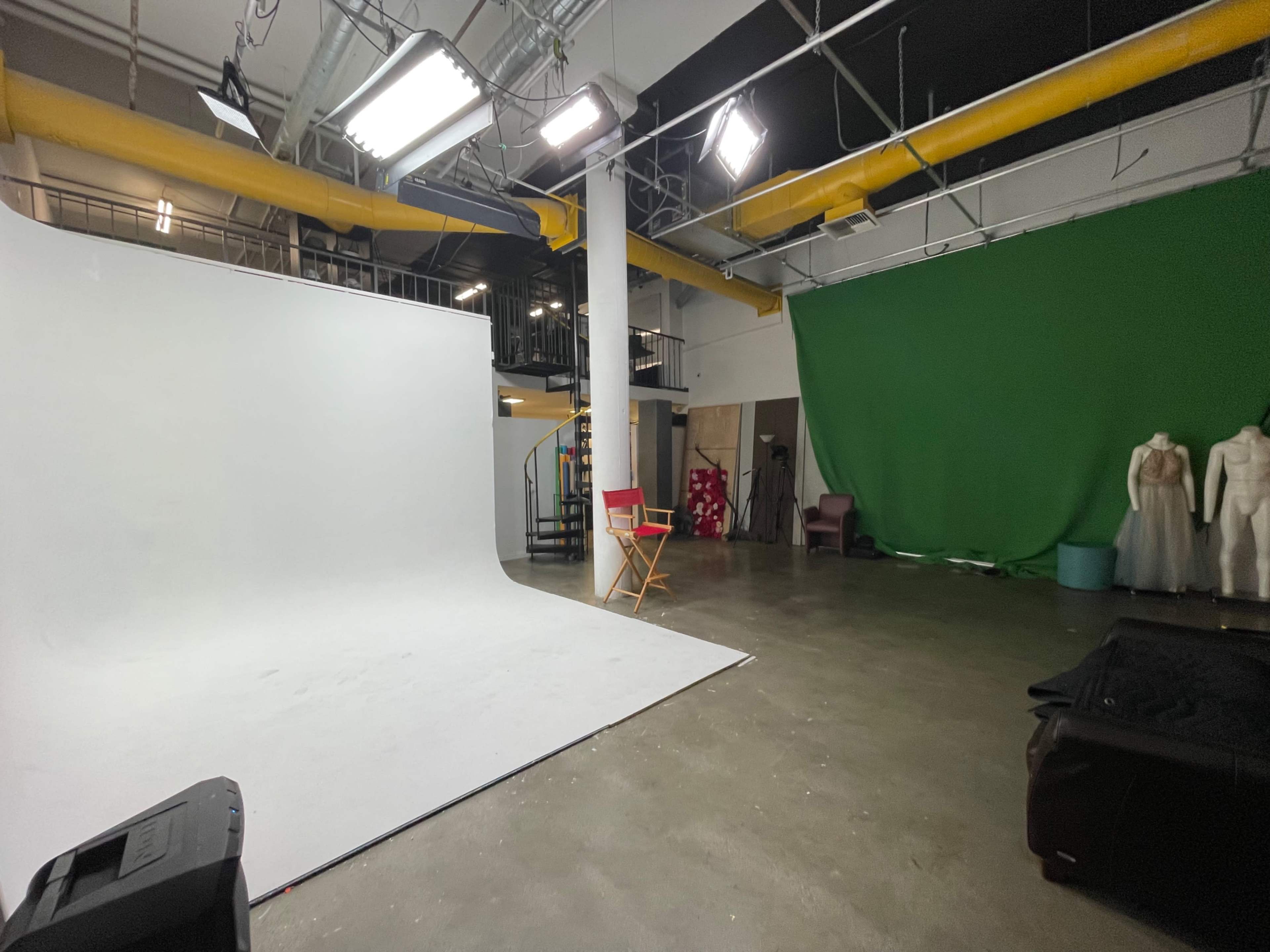 The image shows a photography studio with a white backdrop on one side, a green backdrop on the other, studio lights overhead, and various props and furniture in the space.