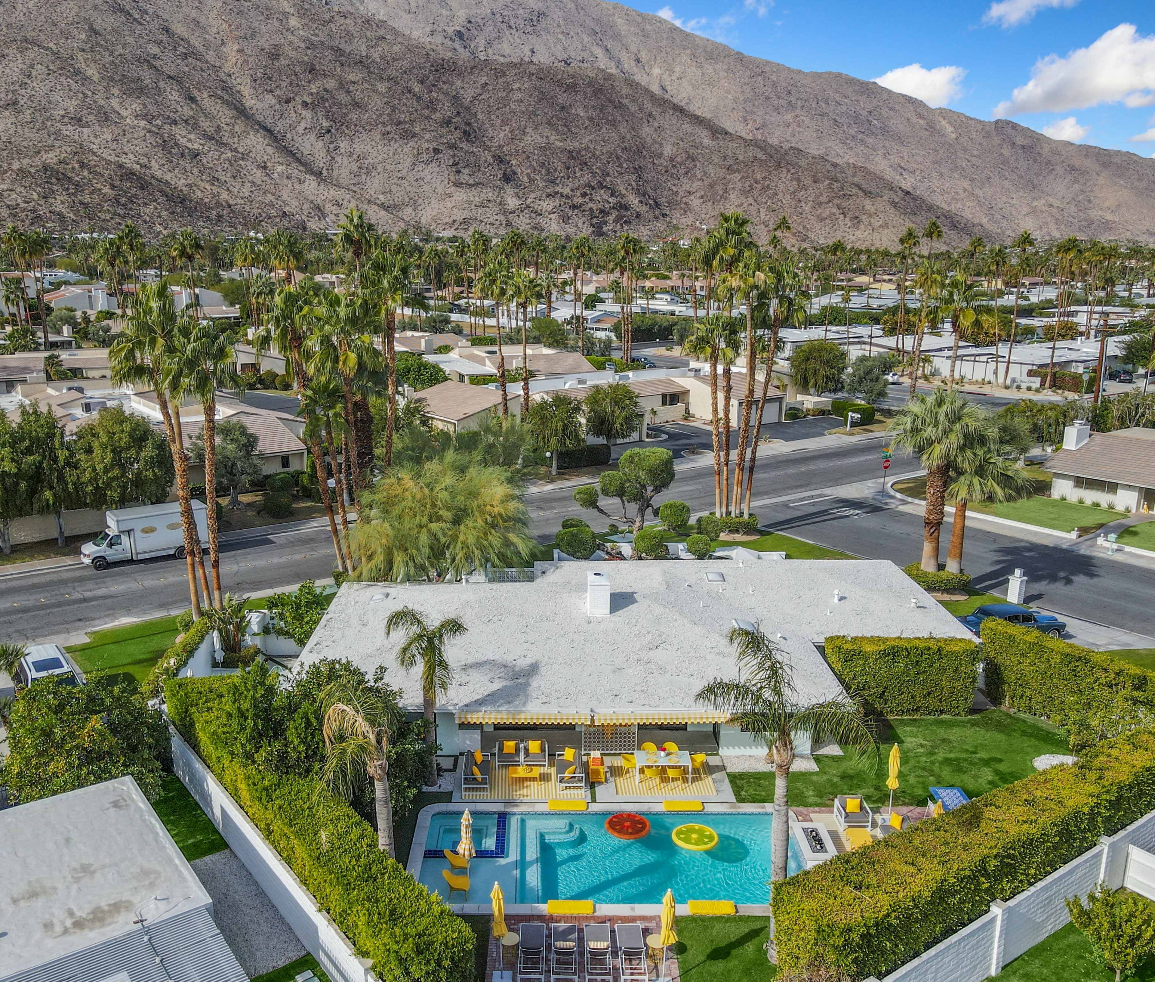 A residential area featuring a swimming pool surrounded by palm trees and a view of mountains in the background.