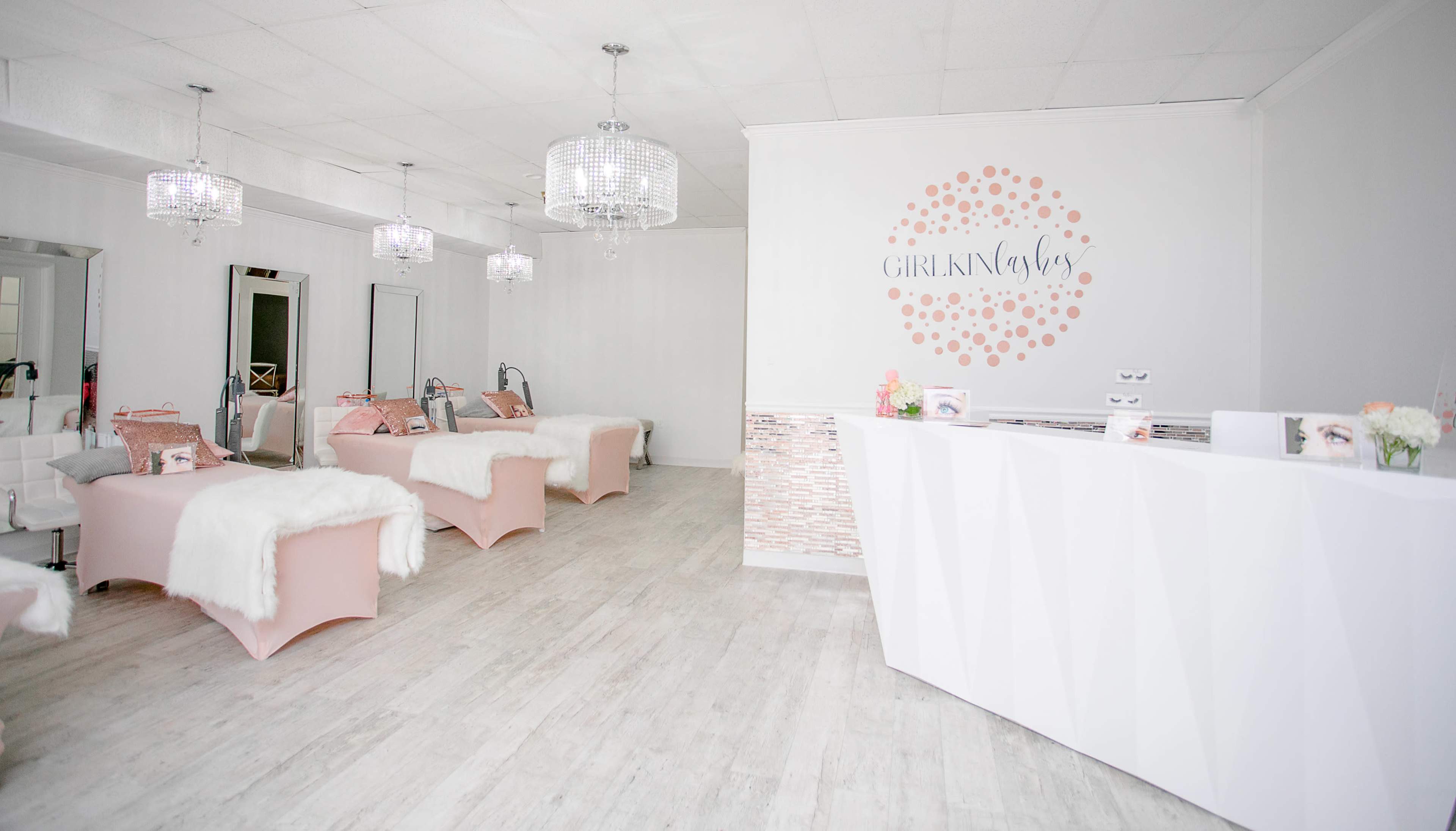 A spacious, well-lit beauty salon with white walls, pink treatment beds, and a reception area featuring a stylish counter and decorative accents.