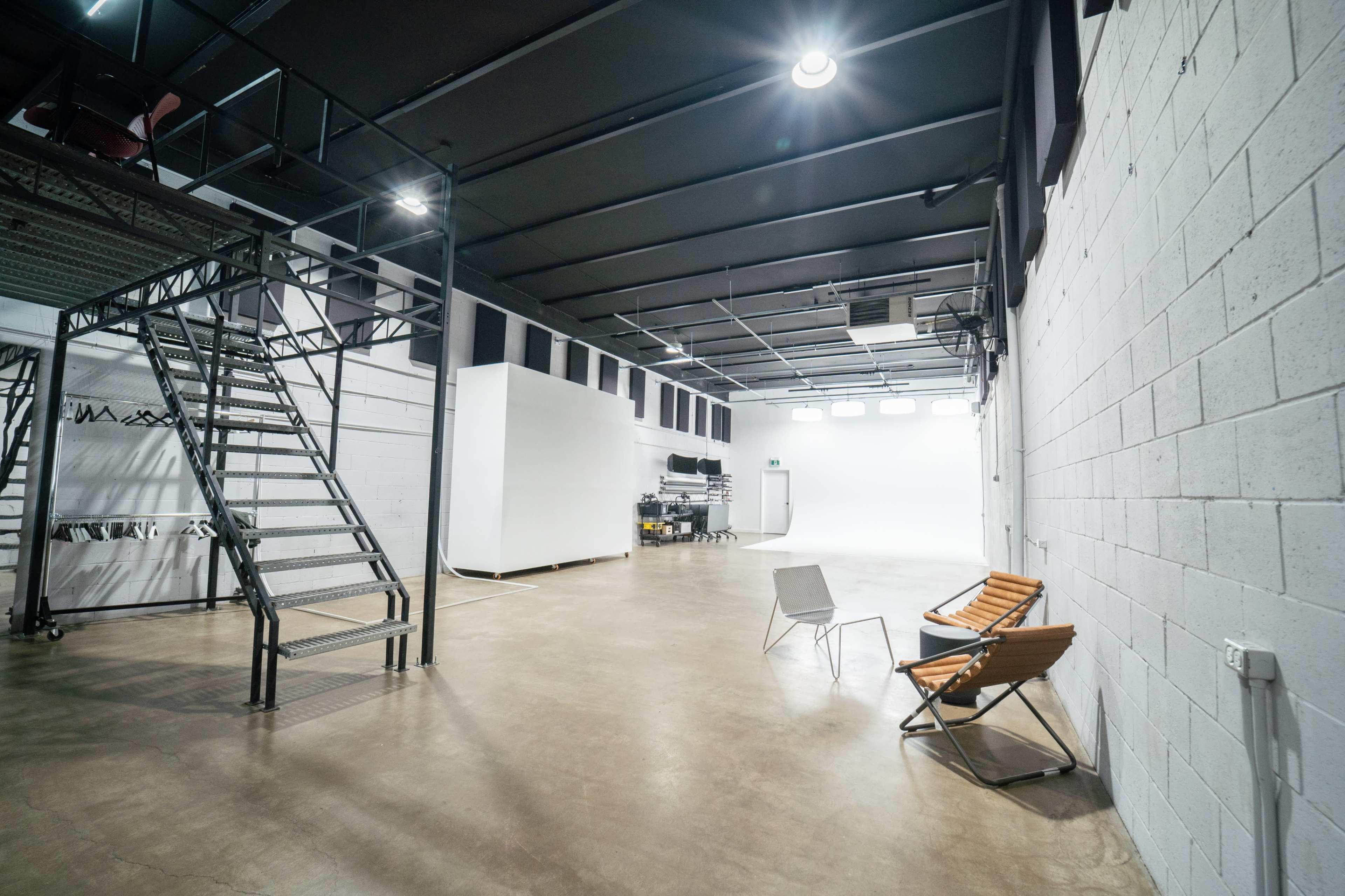 A spacious, industrial-style room with concrete walls, a staircase, and two folding chairs.