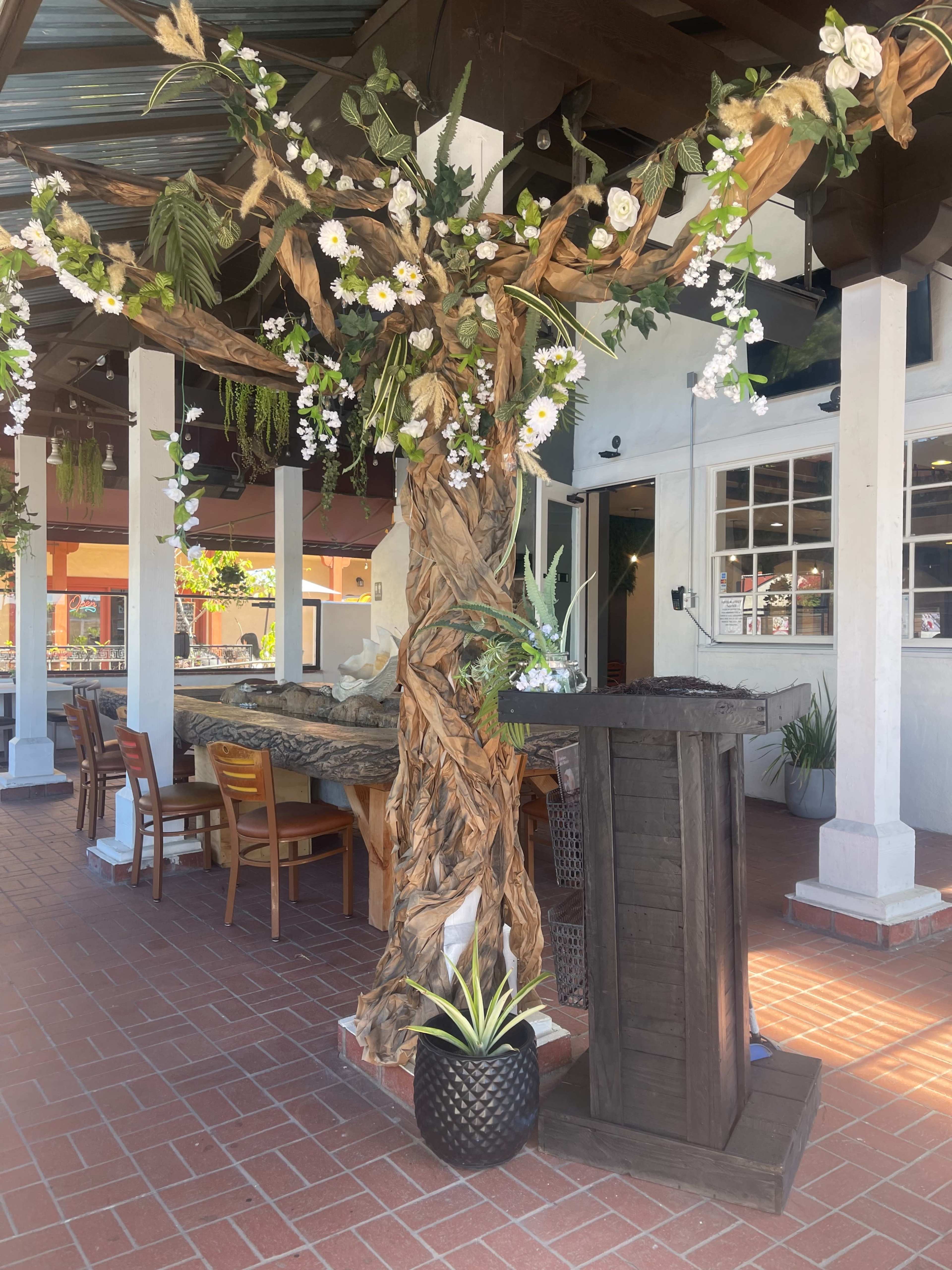 A decorative tree made of twisted branches and adorned with flowers, positioned near a seating area in a restaurant.